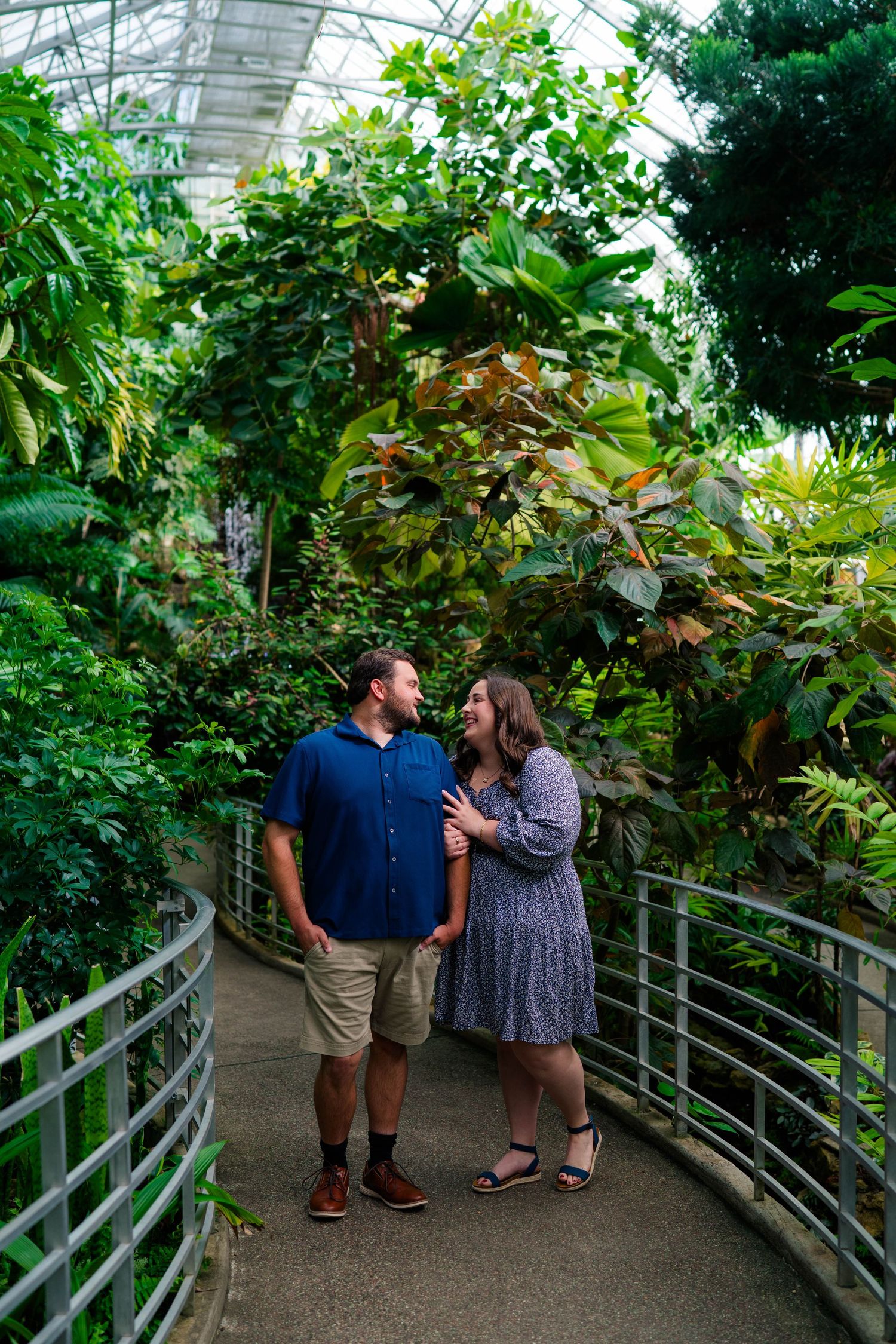 Couple laughing together while walking along a railed path in a tropical greenhouse.