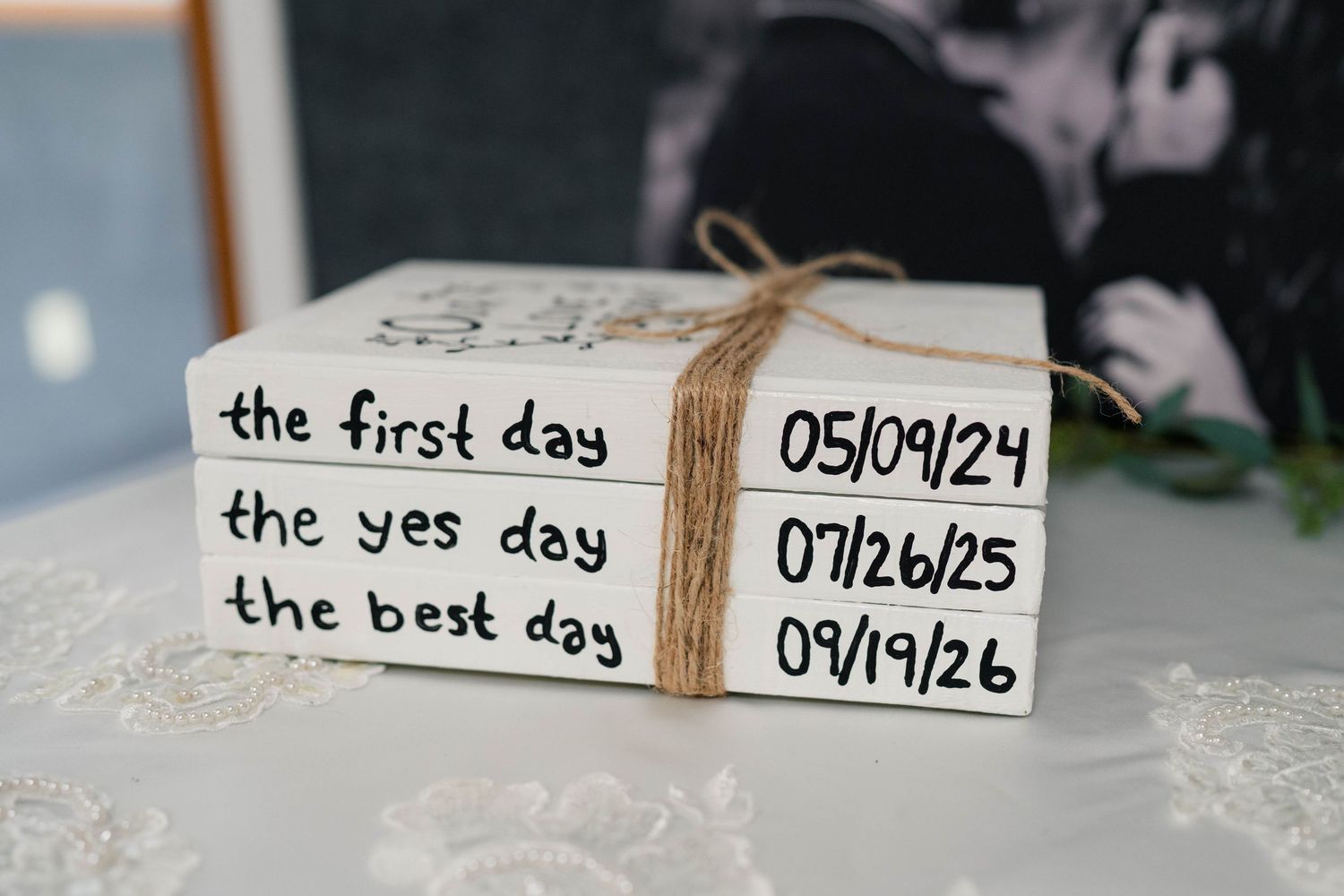 Decorative stacked books display three meaningful couple dates tied with twine as a wedding keepsake centerpiece.