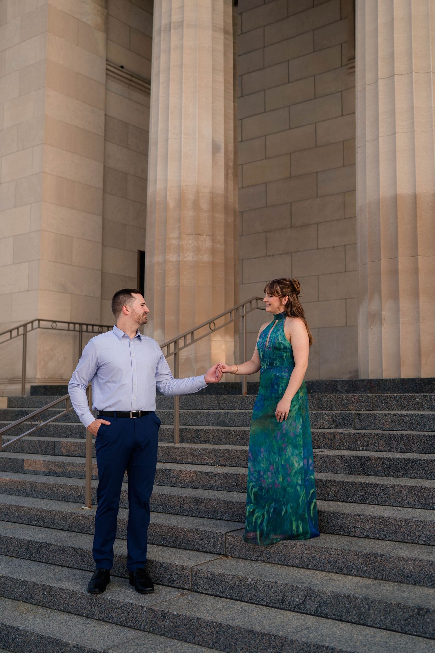 Couple holds hands on wide stone steps flanked by tall pillars of a neoclassical building.