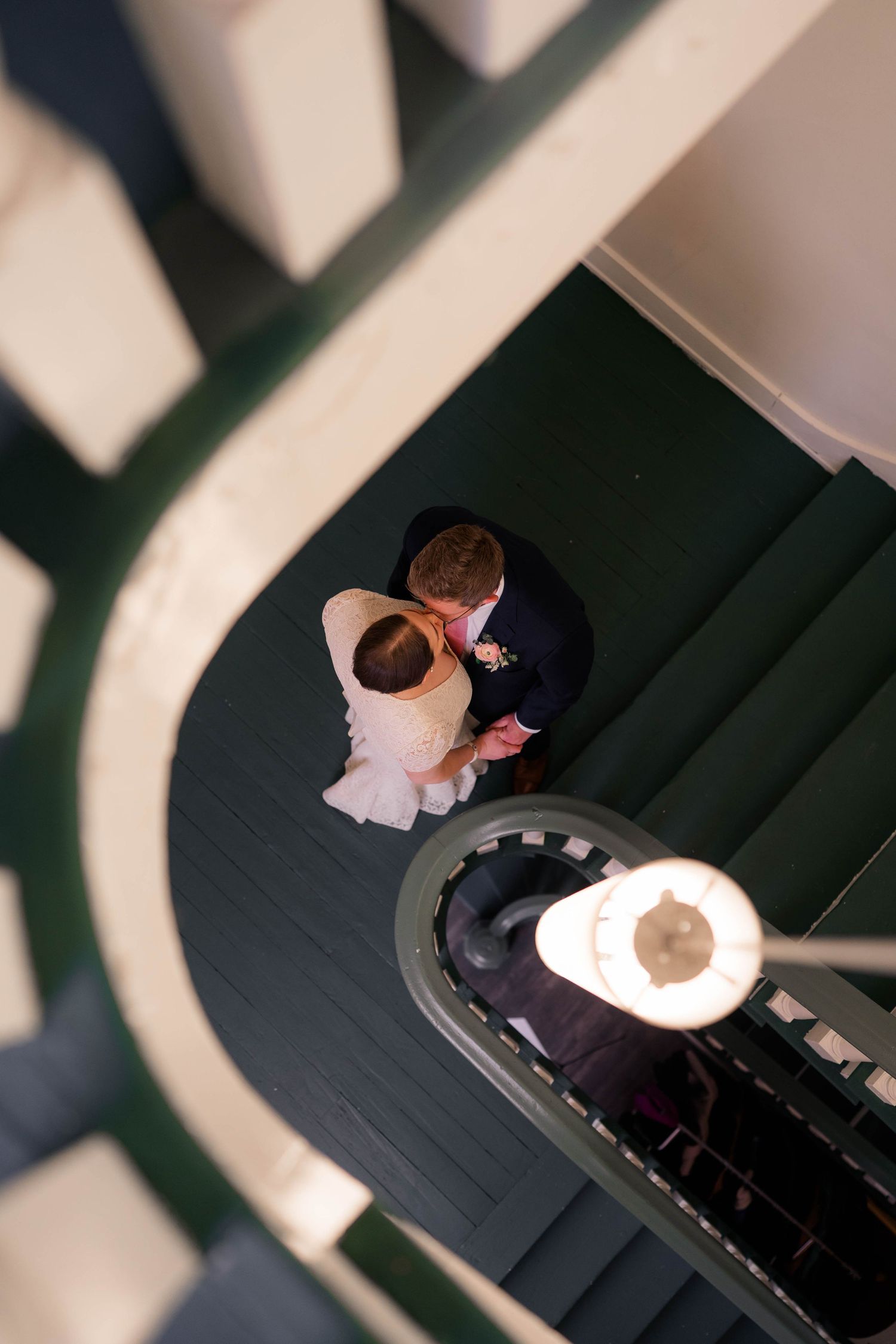 Aerial view of a bride and groom embracing on a green spiral staircase.