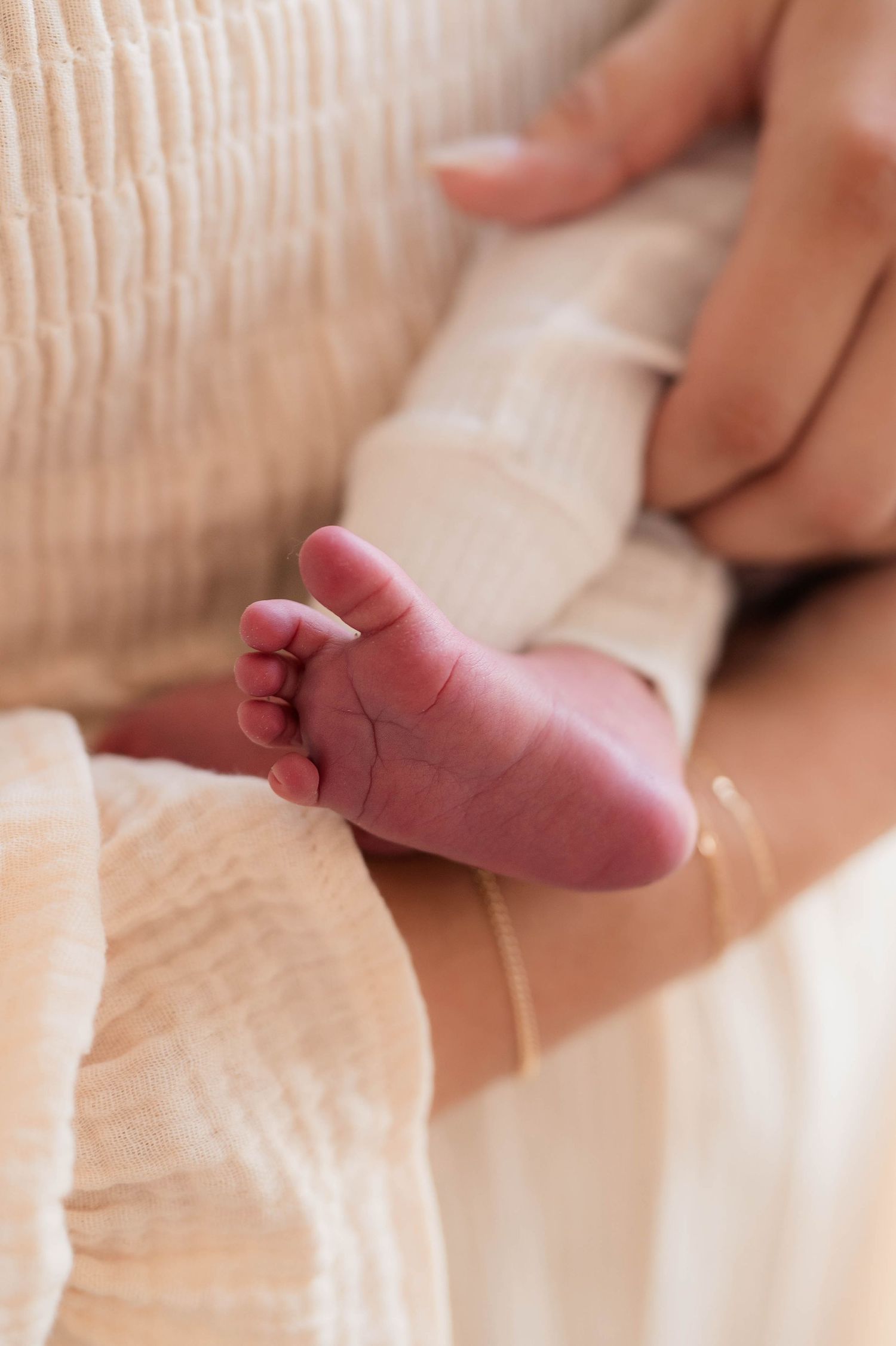 Close-up of a tiny newborn baby foot resting gently in a parents hands on a soft blanket.
