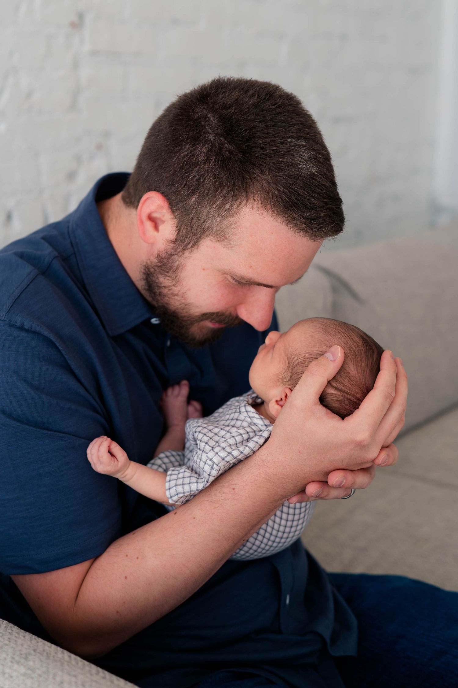 A bearded father in a blue shirt tenderly nuzzles his sleeping newborn baby with love.