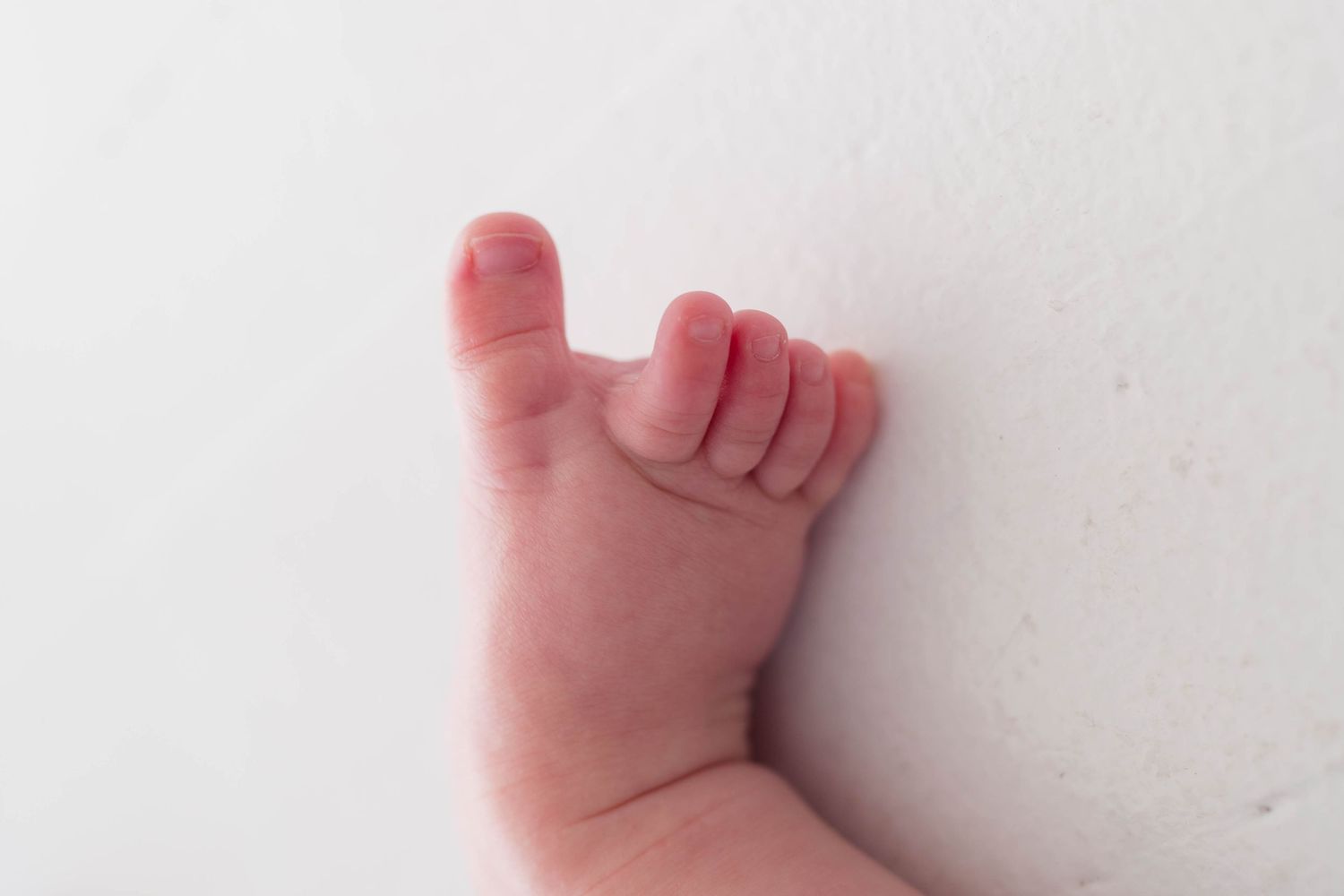 Close-up of a newborn baby's tiny foot and toes resting on a white surface.