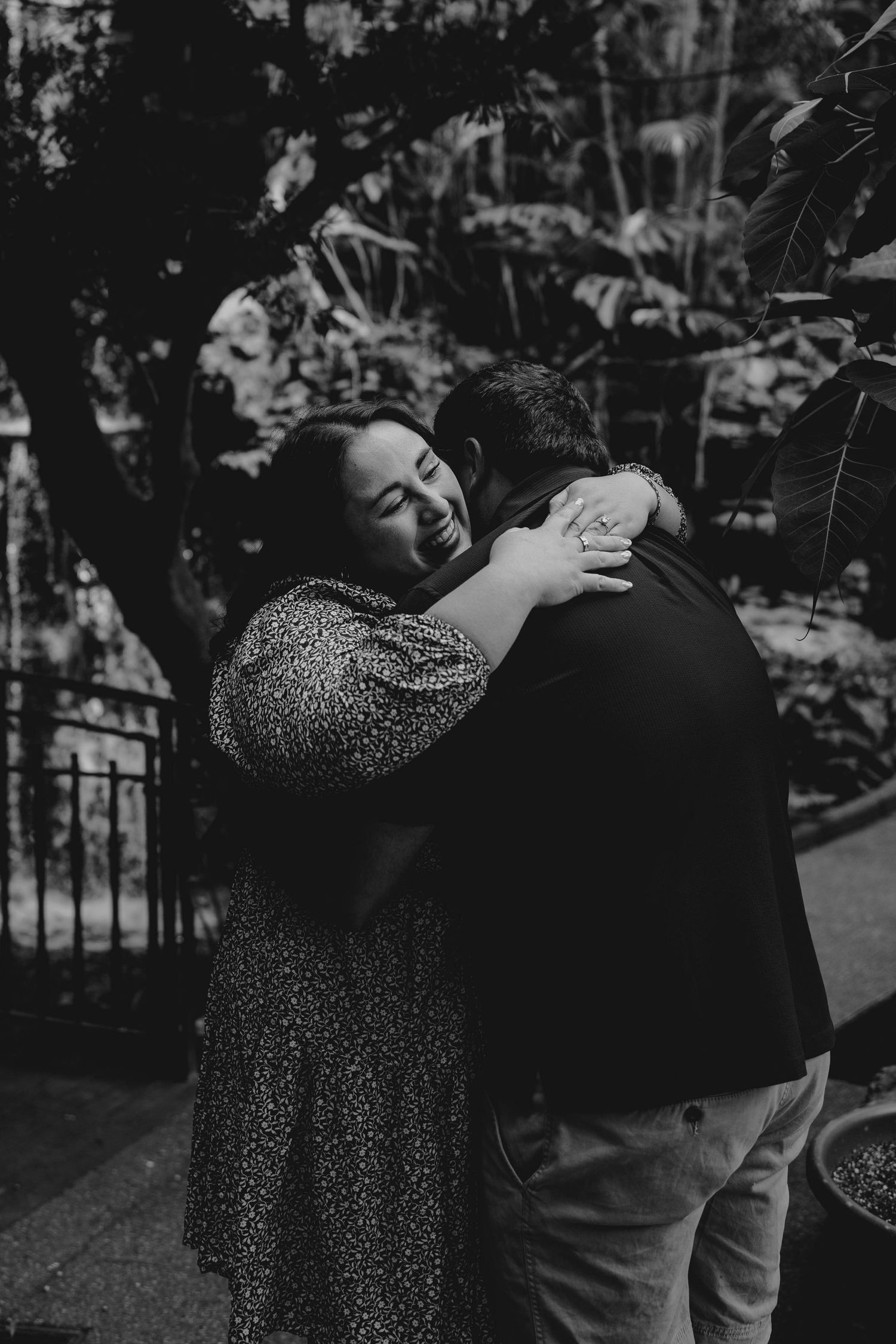 Black and white photo of newly engaged couple embracing joyfully in a lush botanical garden setting.