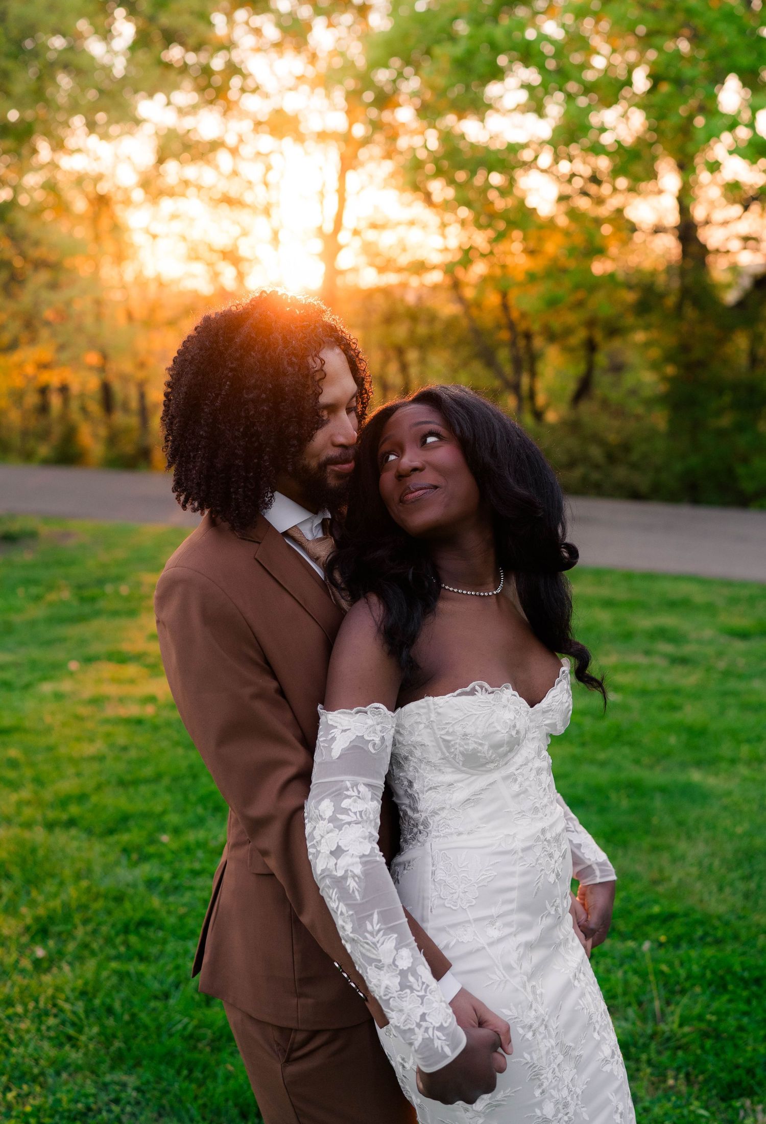 Romantic couple in wedding attire gazing at each other during golden hour in a park setting.