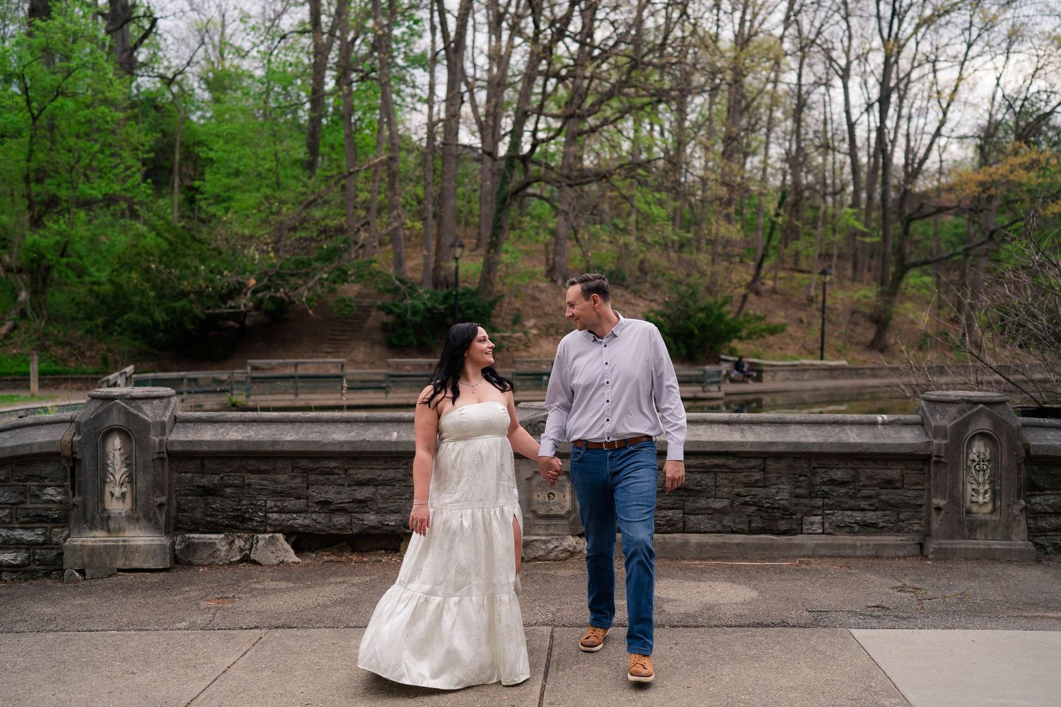 Smiling couple walks hand in hand past stone amphitheater steps during outdoor engagement photo session.