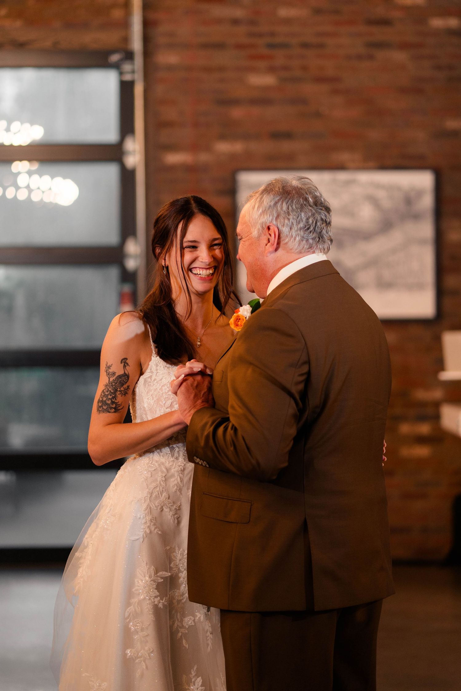 Bride in lace gown shares first dance with father at rustic brick wedding venue.