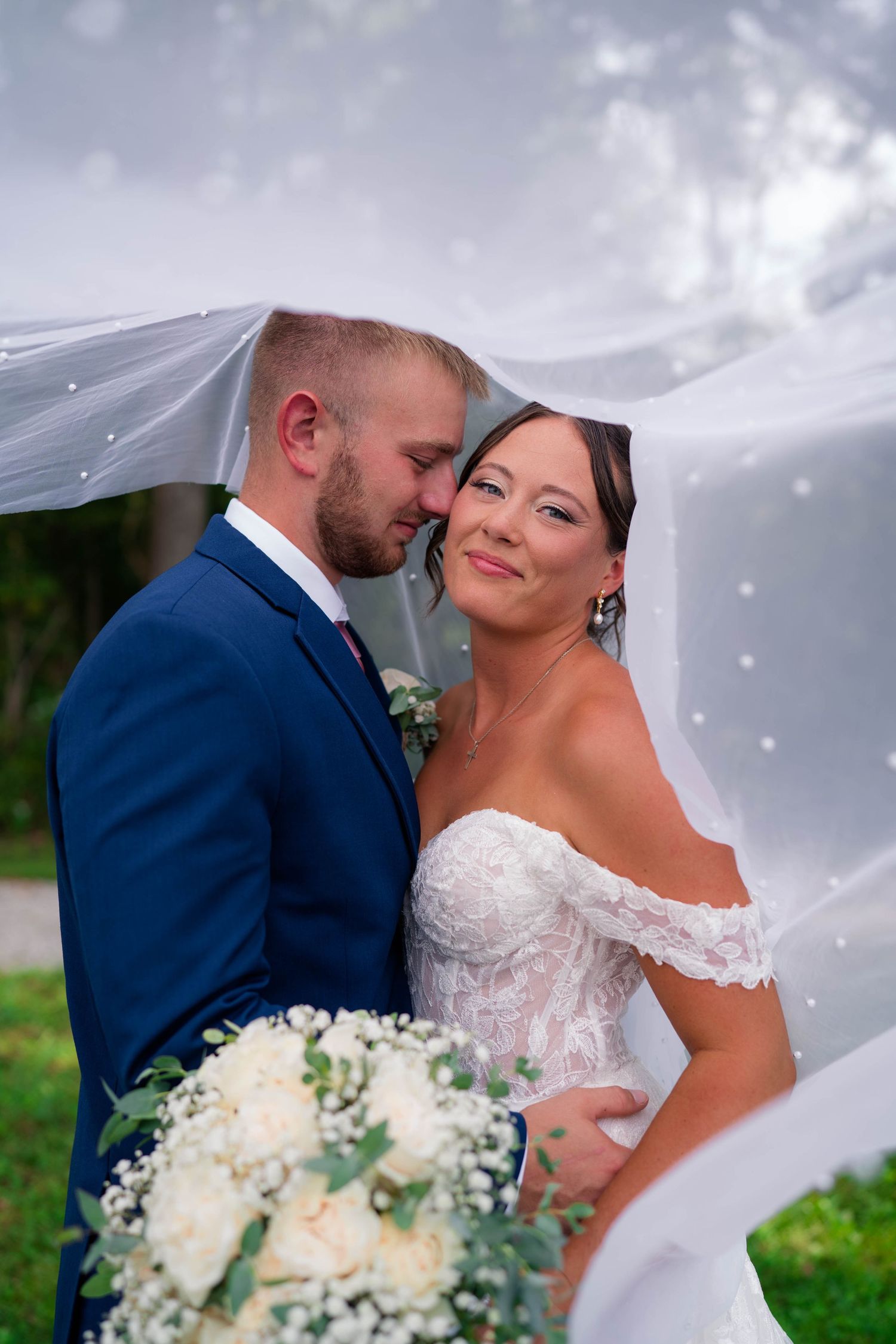 Bride and groom share a romantic moment under a flowing veil outdoors on their wedding day.
