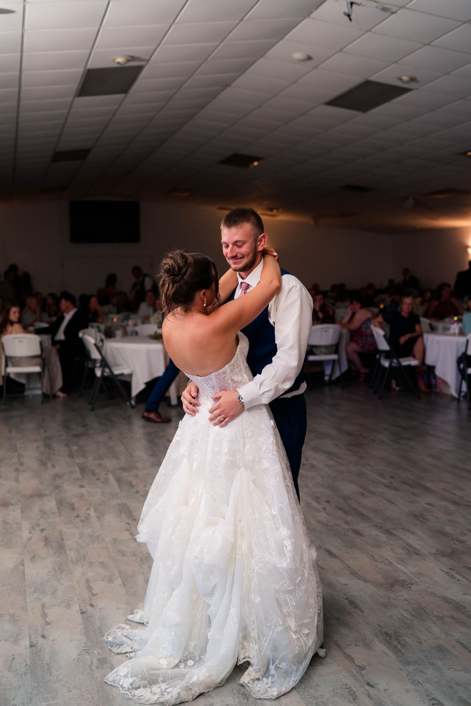 Bride and groom share their first dance at wedding reception, smiling couple embrace on dance floor.