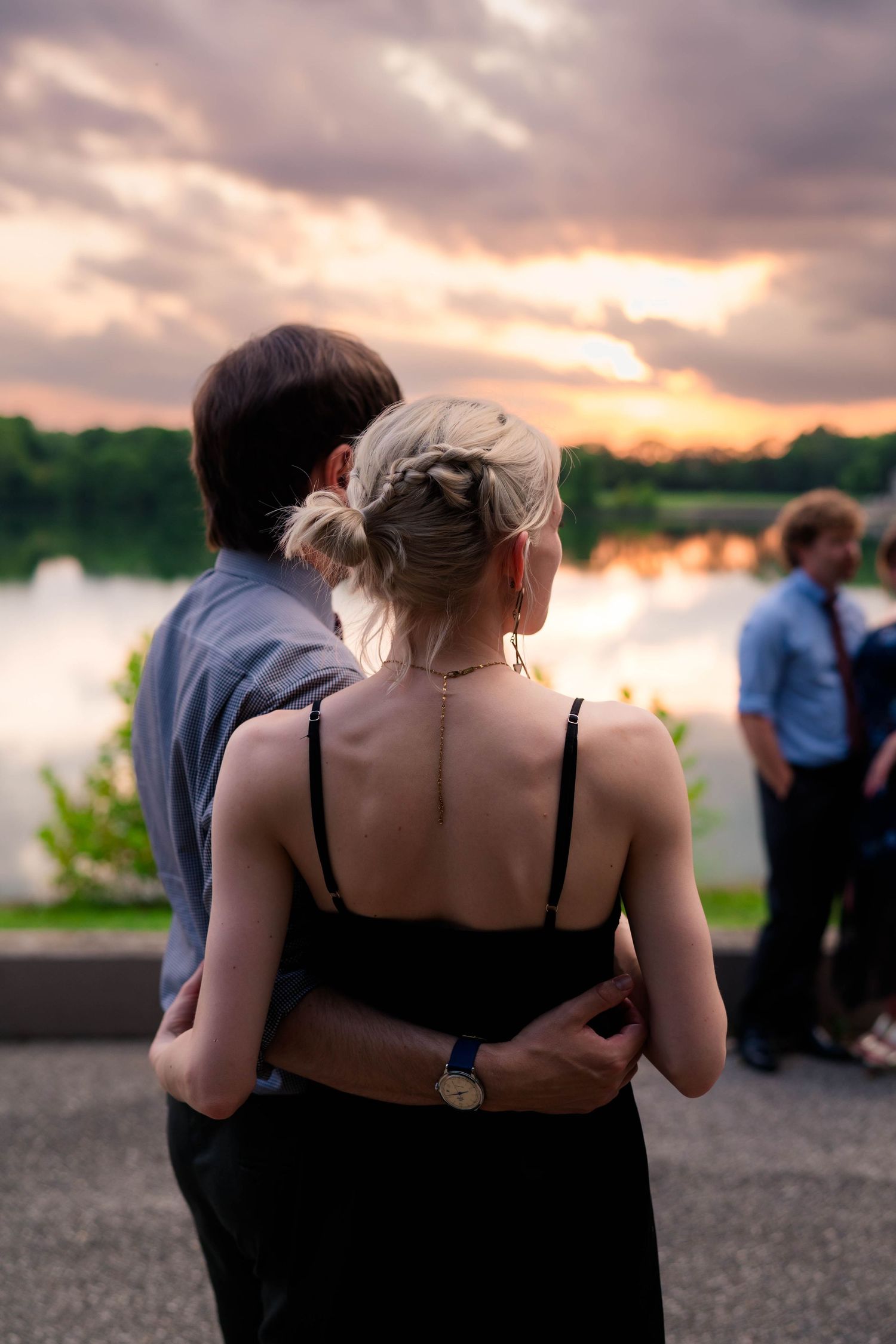Couple embracing while watching a stunning sunset over a lake at a wedding.