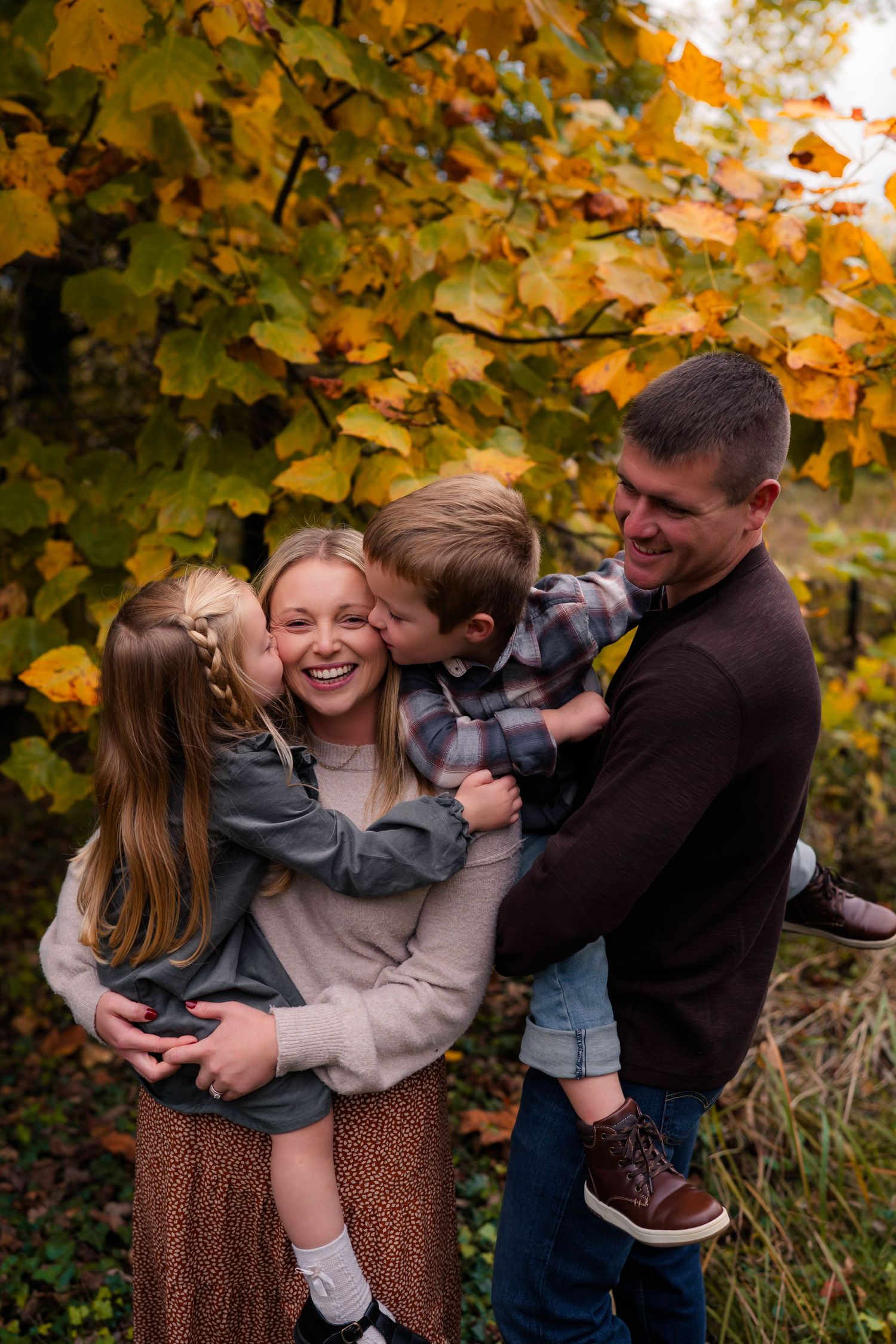 Joyful family of four laughs together under vibrant yellow fall leaves in an outdoor setting.