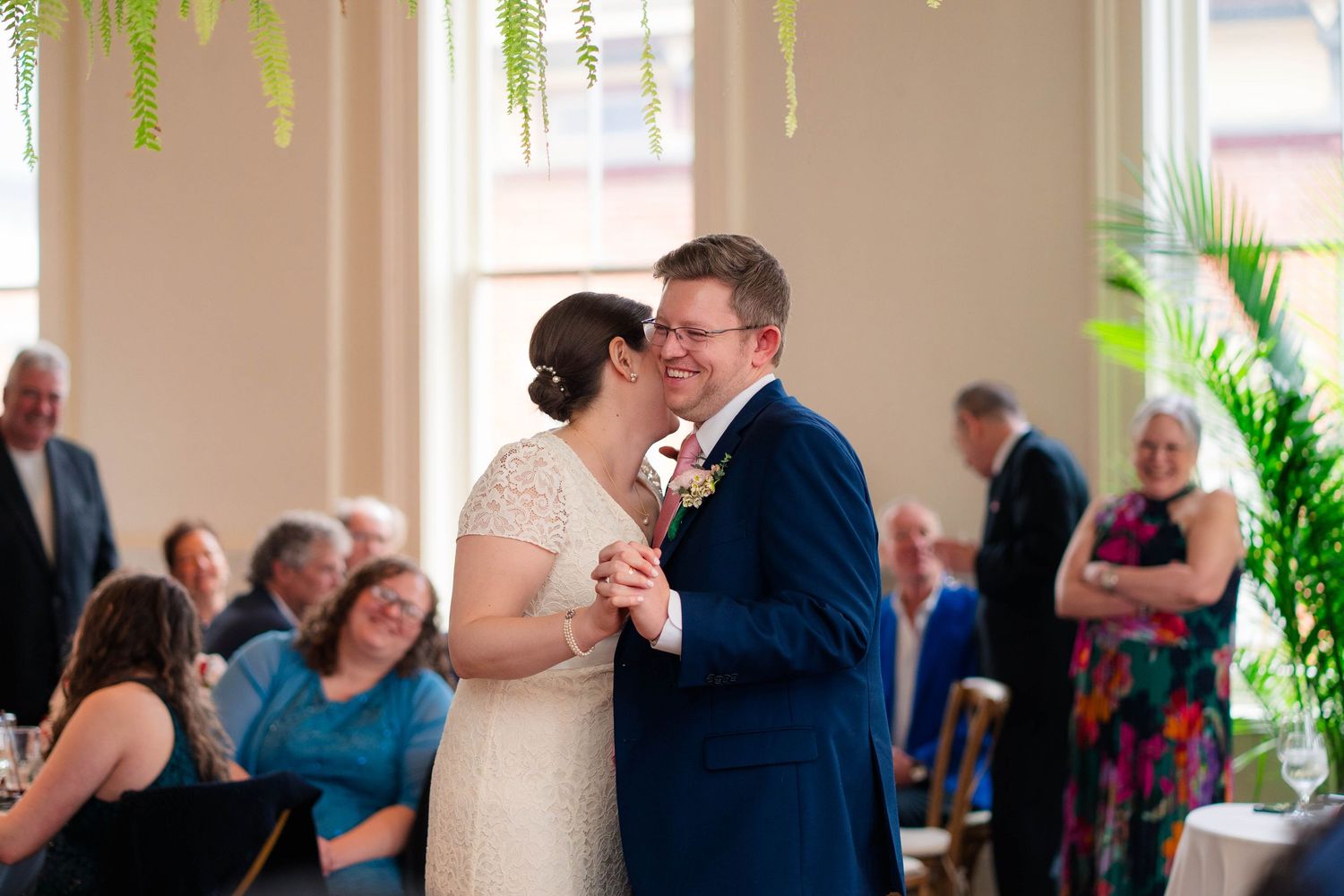 Newlyweds sharing a kiss during first dance with guests watching at wedding reception.