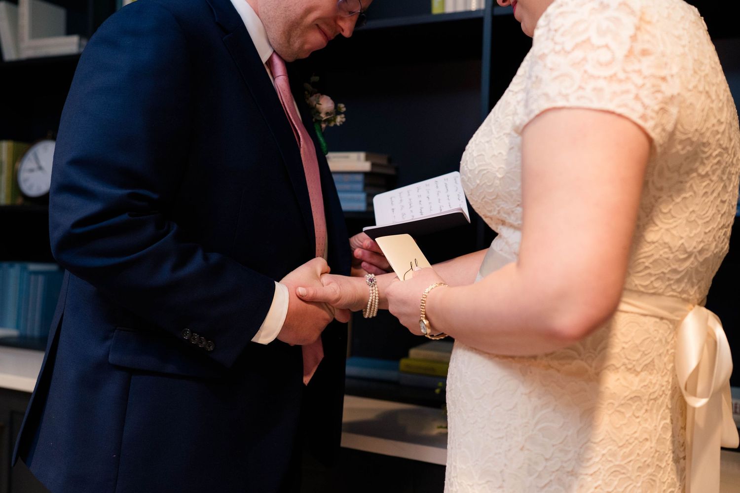 Groom places wedding ring on brides finger during an intimate vow exchange ceremony indoors.