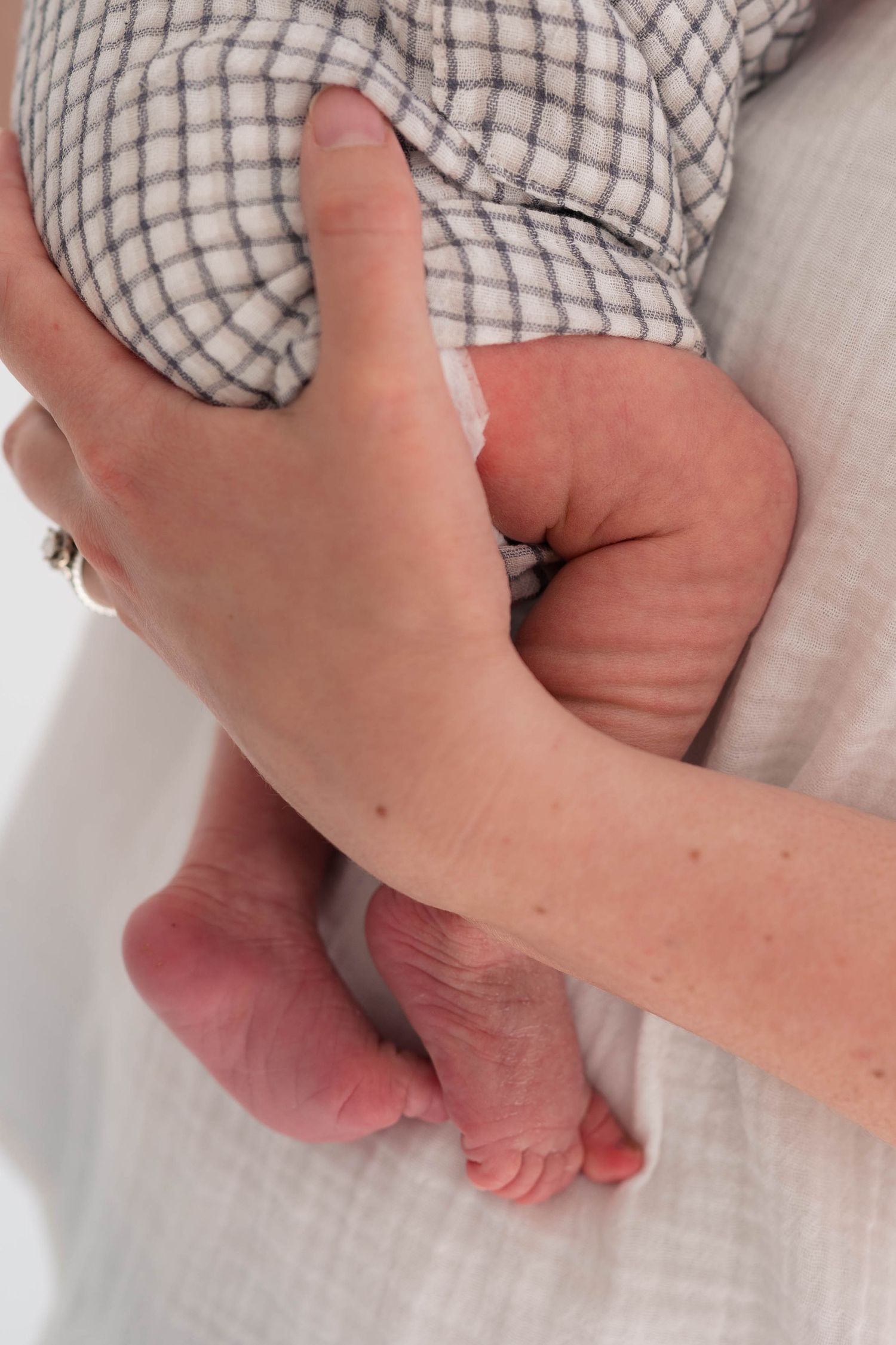 Close-up of adult hands gently cradling tiny newborn baby feet and legs in a plaid outfit.