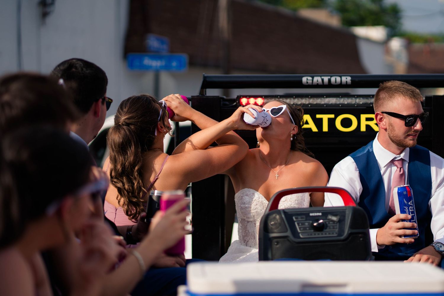 Bride and guests celebrate on Gator vehicle outdoors after summer wedding reception.
