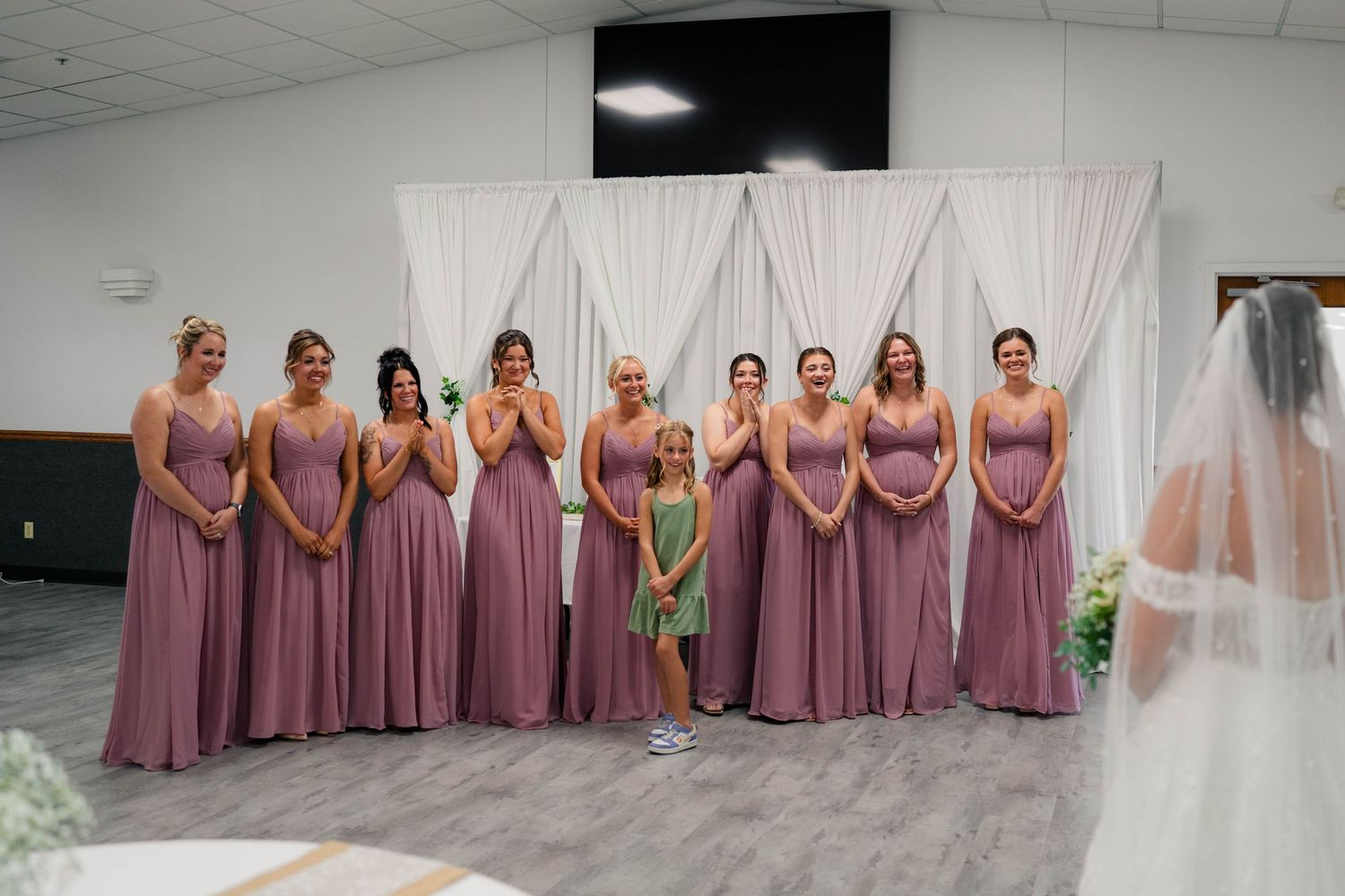 Group of bridesmaids in dusty rose gowns reacting emotionally as bride enters ceremony venue.