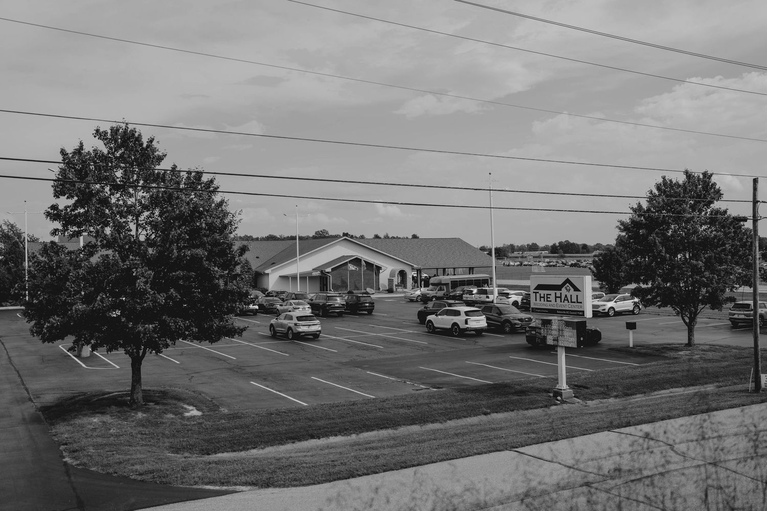 Black and white aerial view of a small commercial building with parking lot and trees on overcast day.