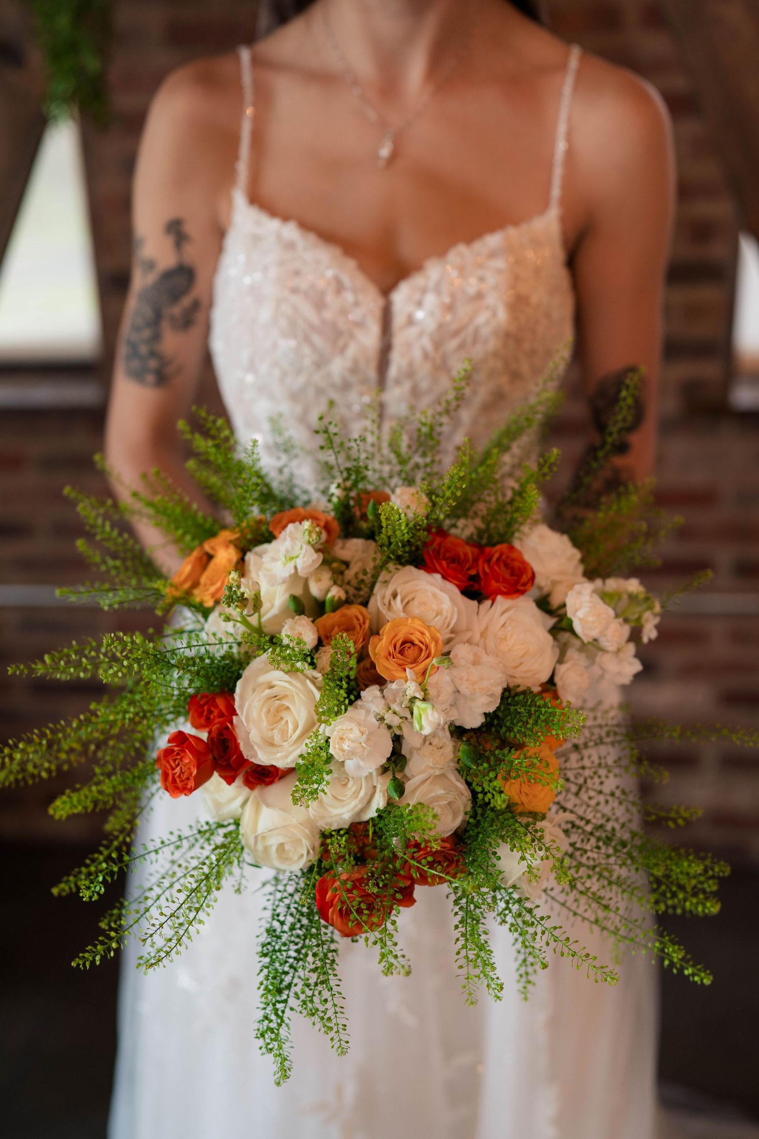 Close-up of lush bridal bouquet featuring white, peach, and red roses with green fern accents.