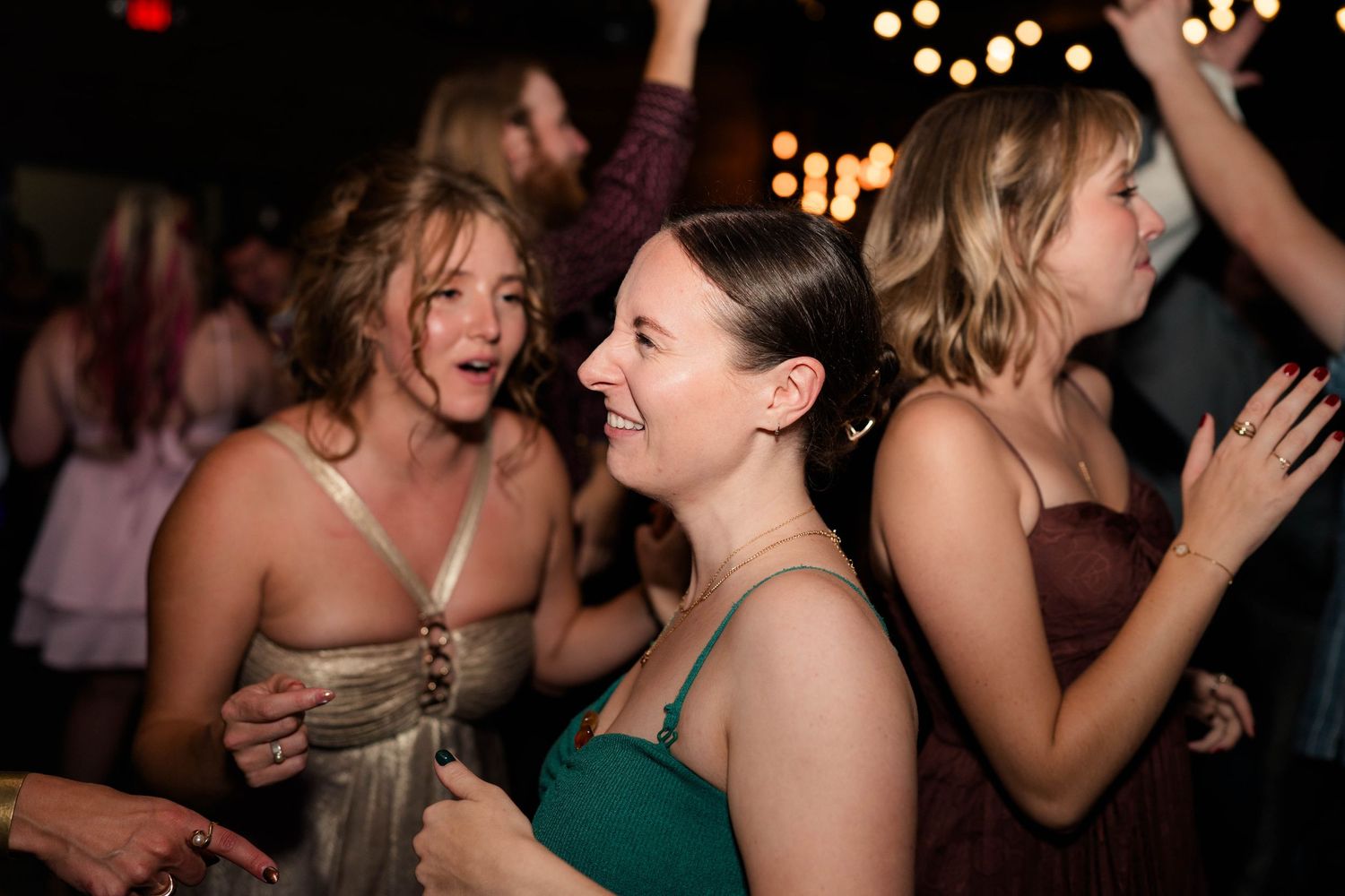 Smiling wedding guests dancing joyfully on crowded dance floor at evening reception.