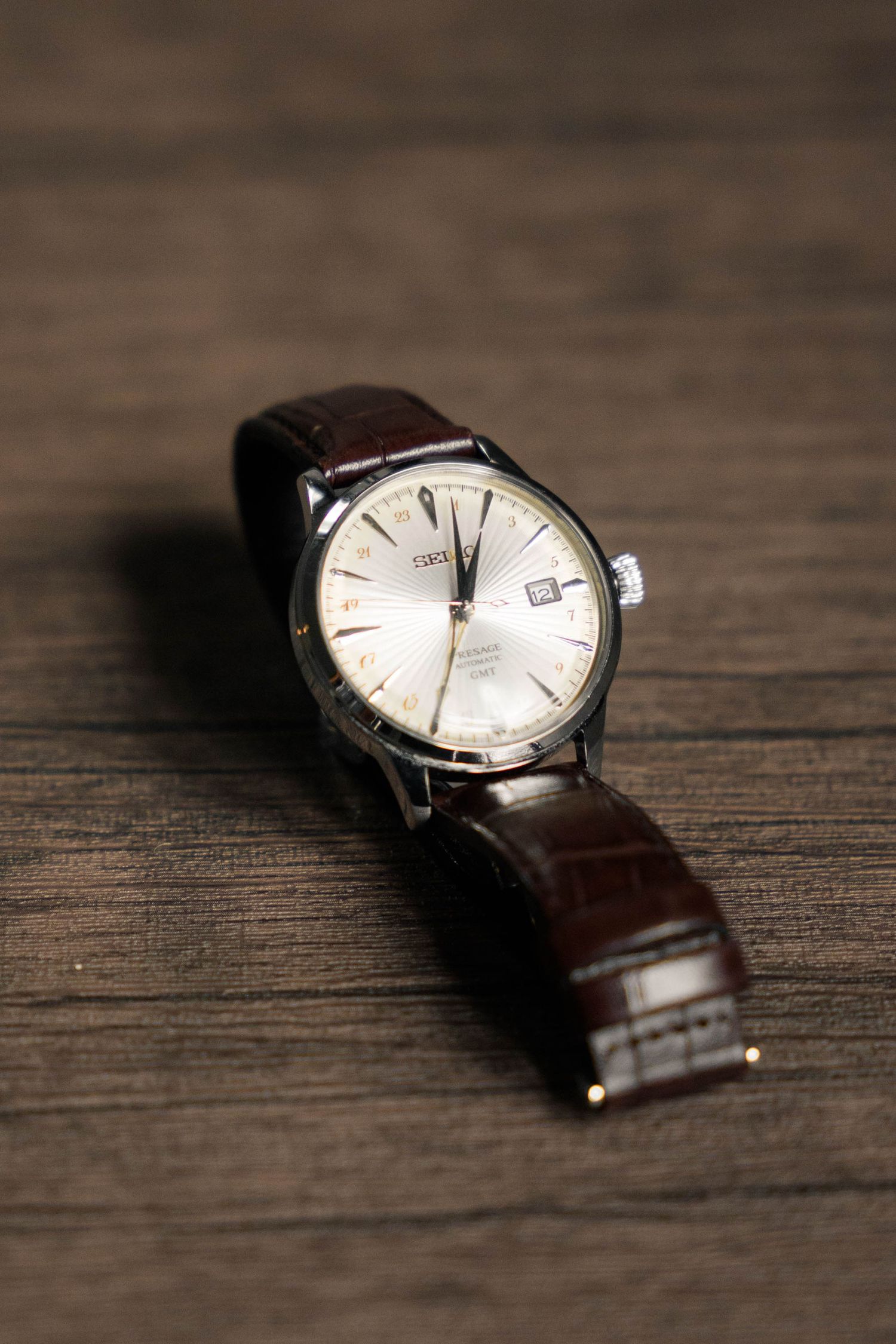 Classic brown leather wrist watch with white dial on wooden surface.