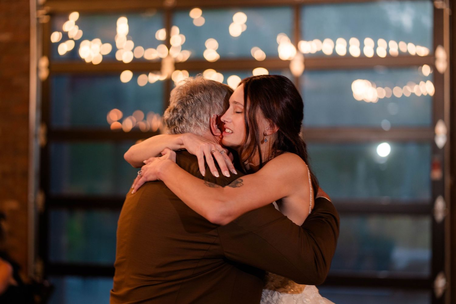 Bride shares tender embrace with father during emotional father-daughter dance at wedding reception.