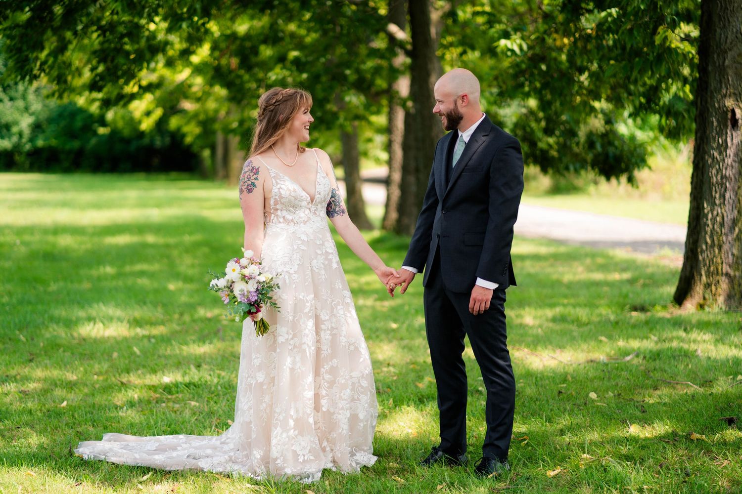 Bride and groom hold hands while walking through sunlit green park together.
