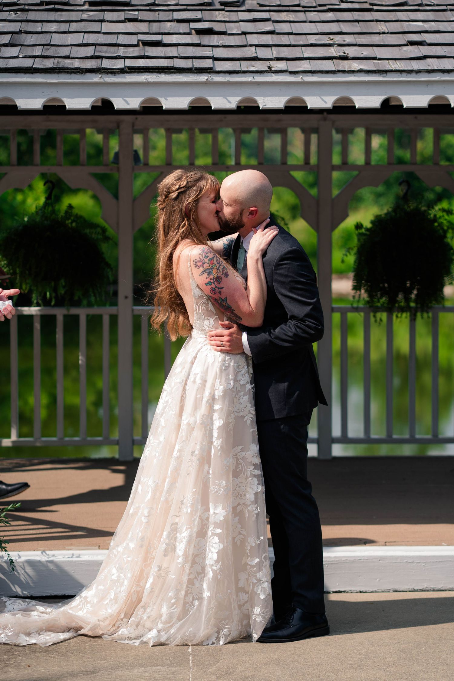 Bride and groom sharing first kiss in front of white gazebo at outdoor wedding ceremony.