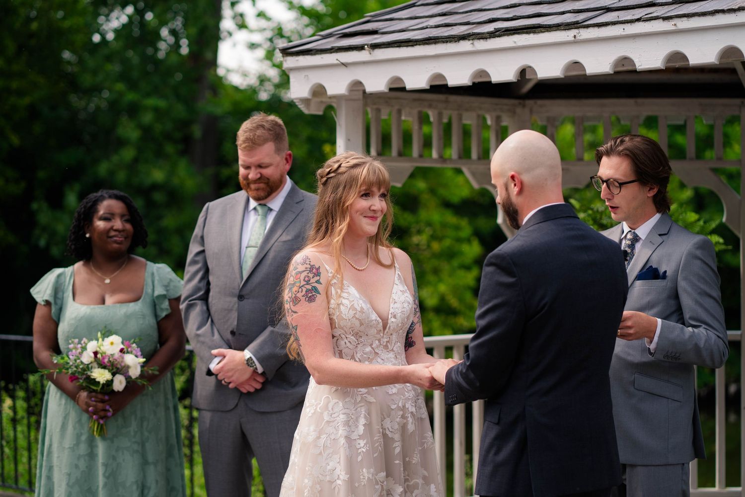 Bride and groom exchange vows outdoors at a garden wedding ceremony with bridesmaids and groomsmen nearby.