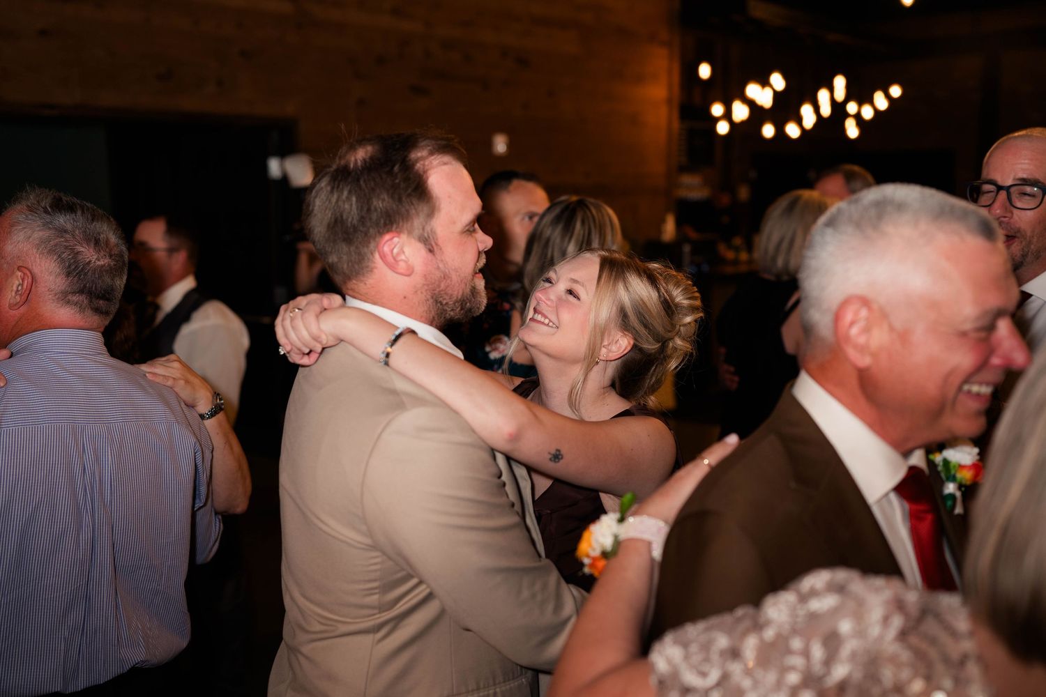 Couple dances closely together smiling at wedding reception under warm string lights.