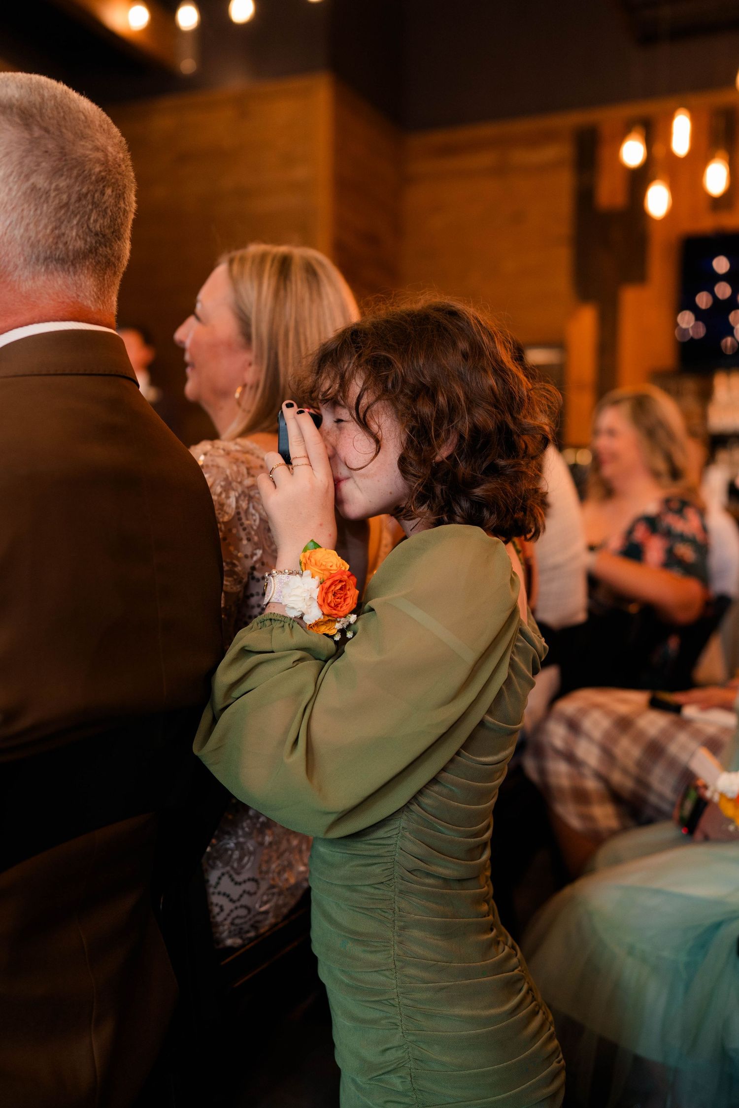 Emotional wedding guest in green dress with orange corsage covers mouth during ceremony.