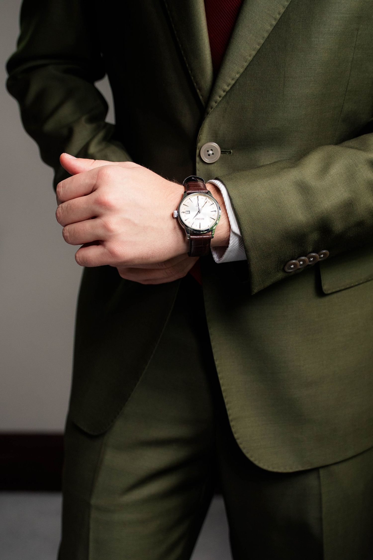 Groom in olive green suit adjusting watch cuff on wedding day.