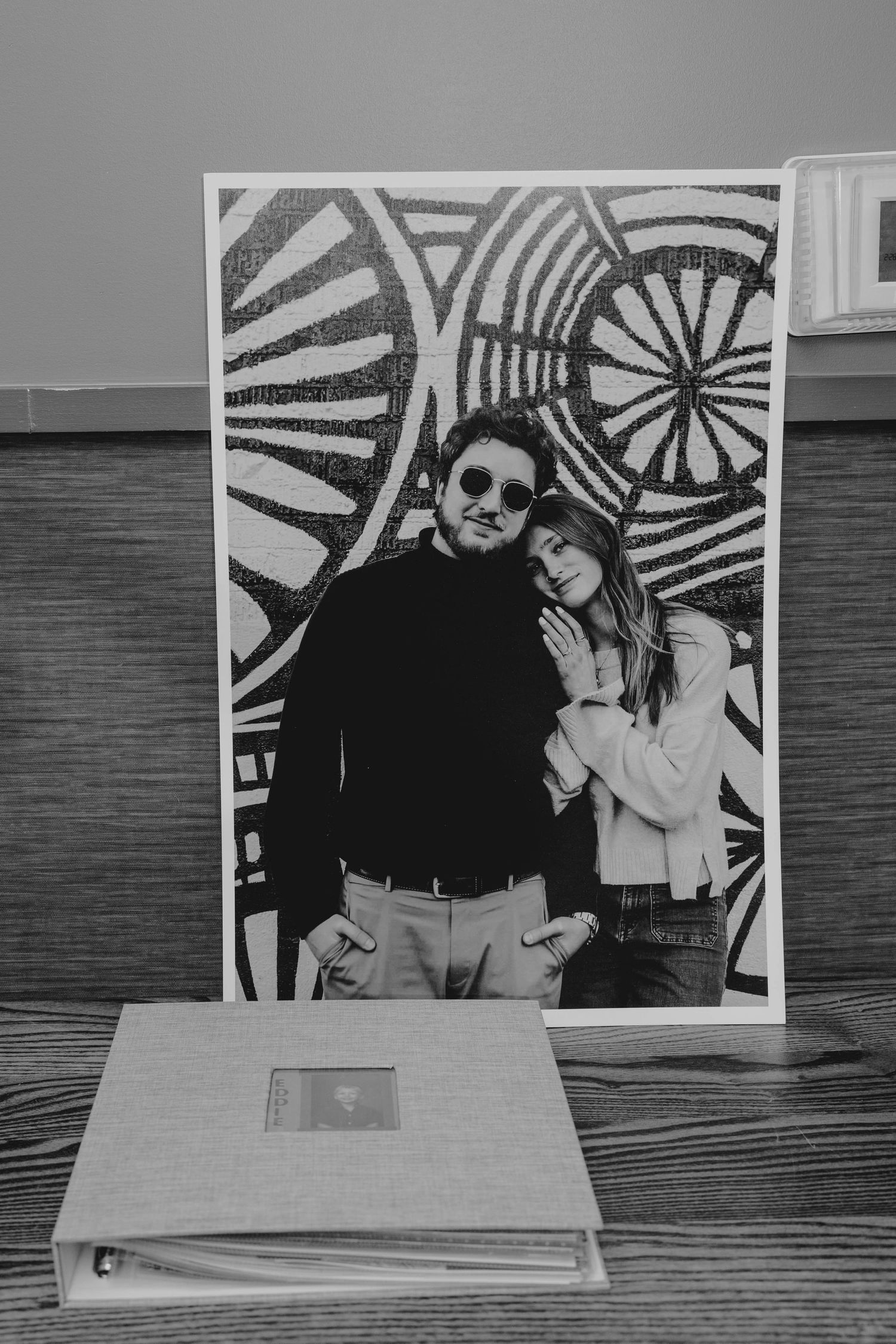 Black and white photo of a framed couple portrait displayed on a wooden table beside a guest book.
