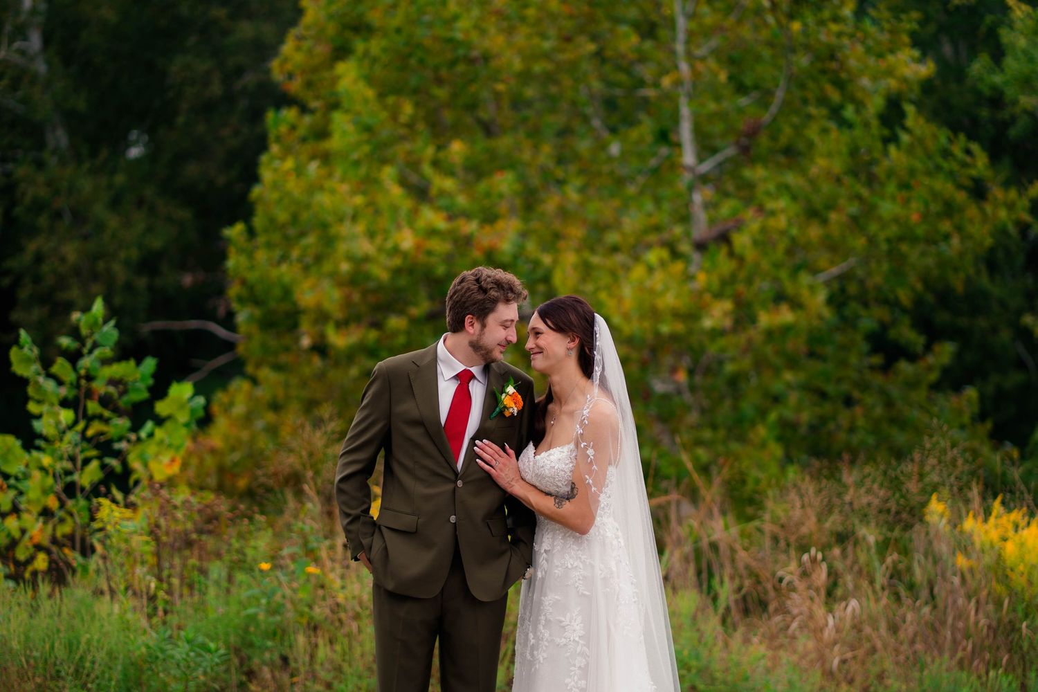 Bride and groom touching foreheads romantically in colorful autumn outdoor setting.