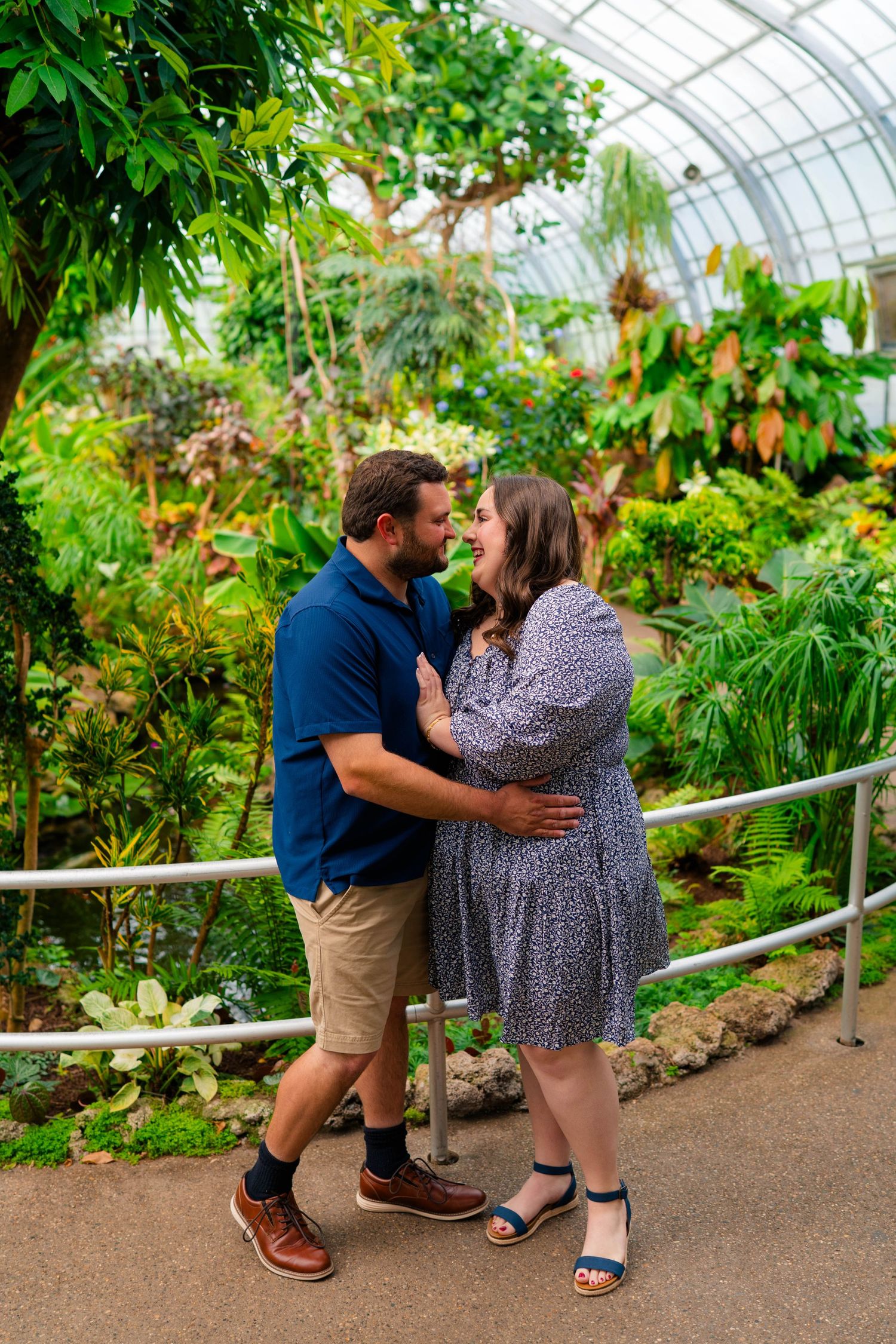 Couple embracing and smiling at each other inside a lush tropical greenhouse conservatory.