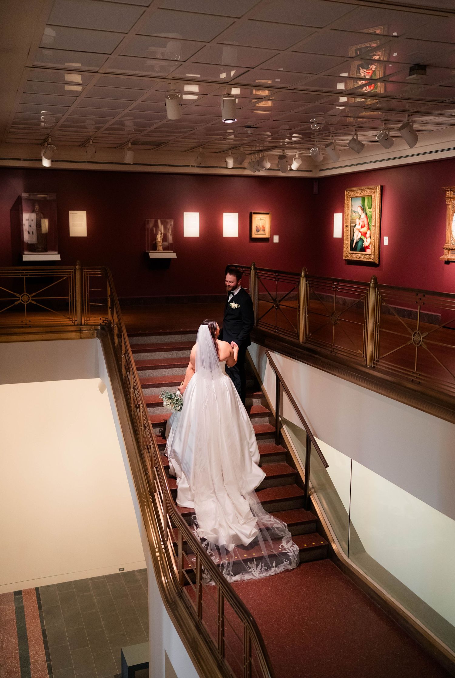 Bride and groom descend a grand staircase inside an elegant art museum wedding venue.