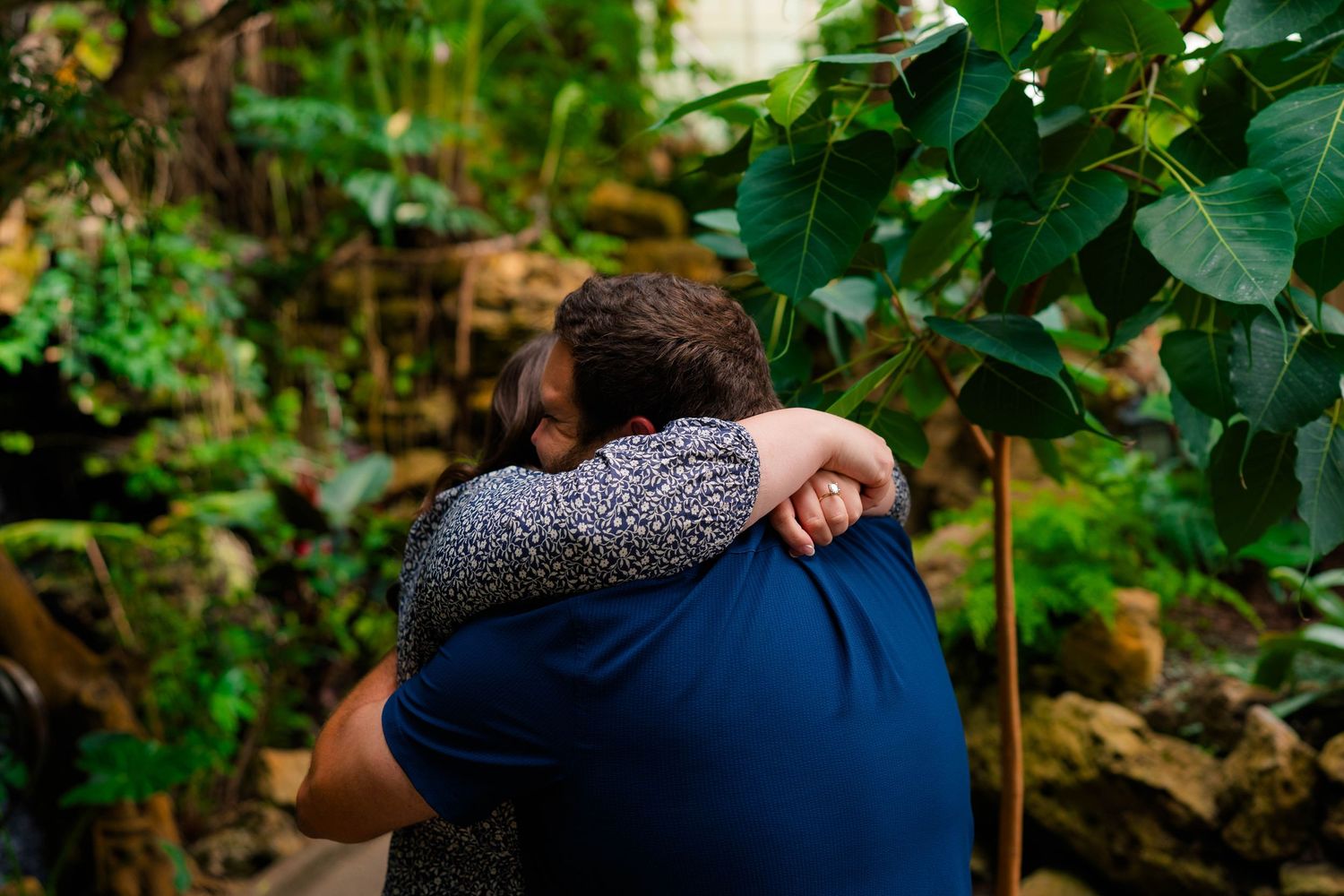 Newly engaged couple sharing a heartfelt embrace surrounded by tropical garden foliage.