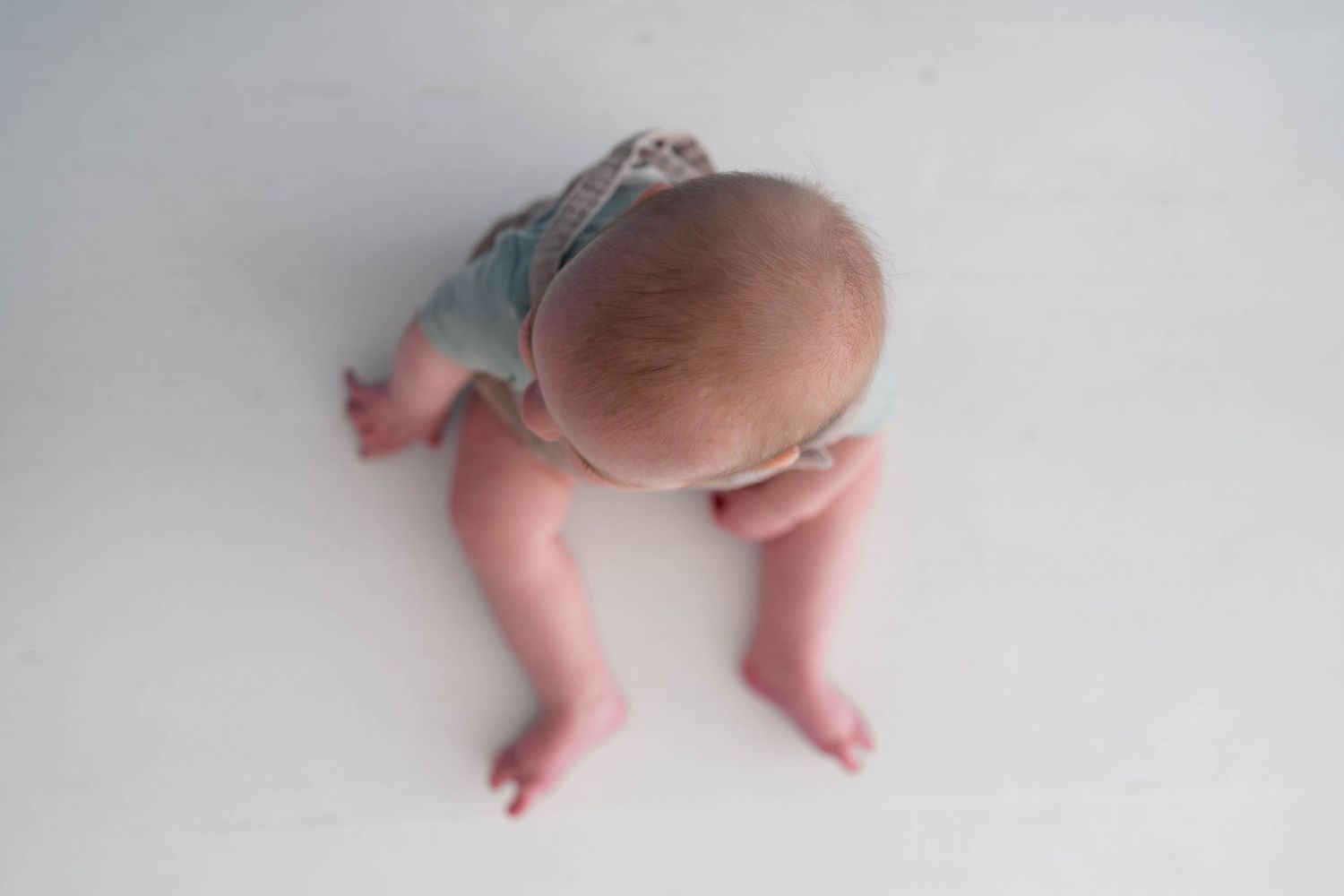 Overhead view of a newborn baby in a denim romper crawling on a white surface.