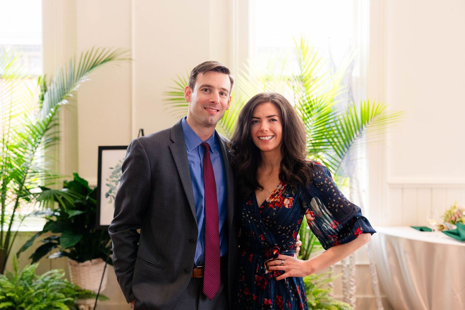 Smiling couple posing together at elegant indoor event with tropical plants.