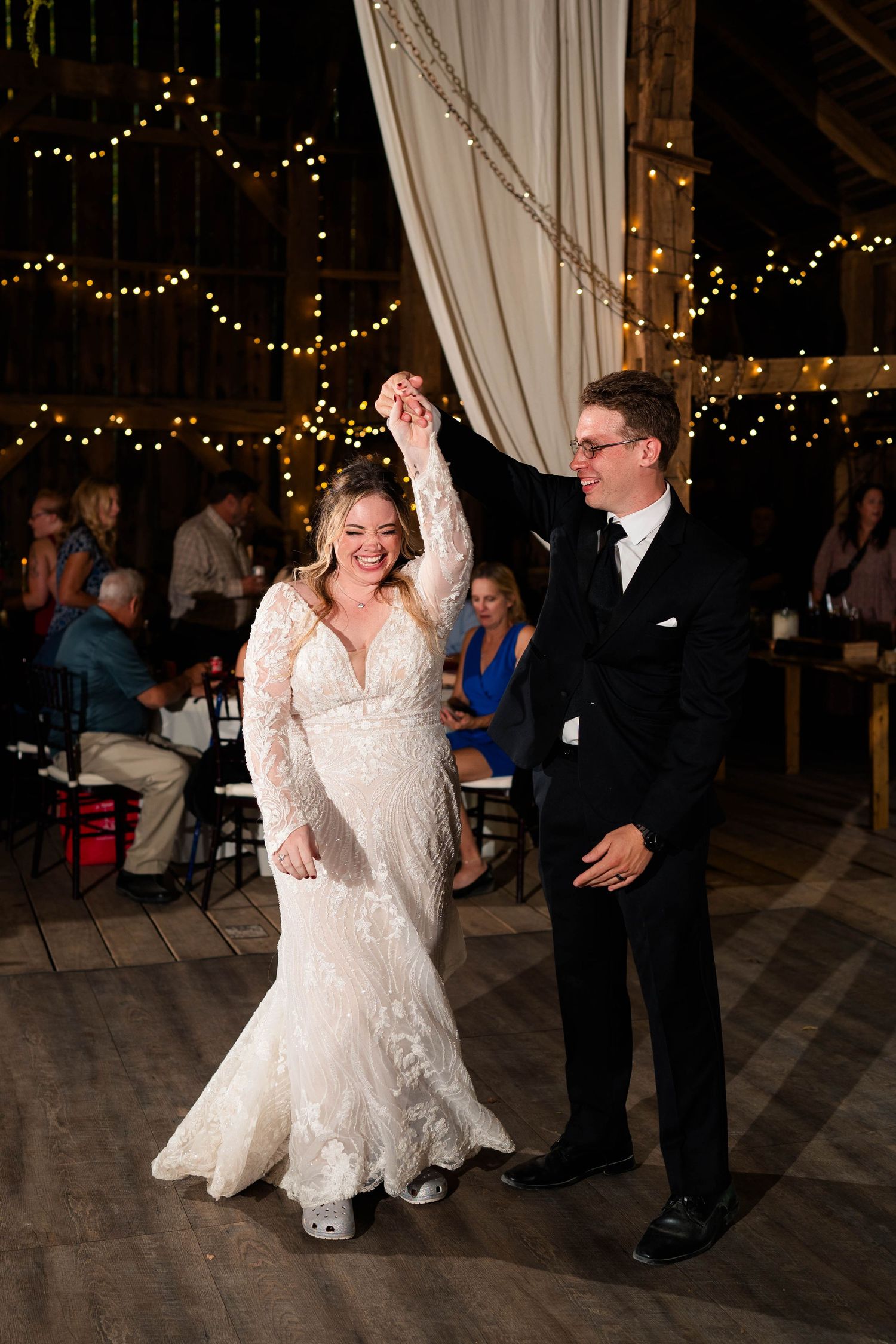 Bride and groom share first dance under twinkling string lights in a rustic barn wedding reception.