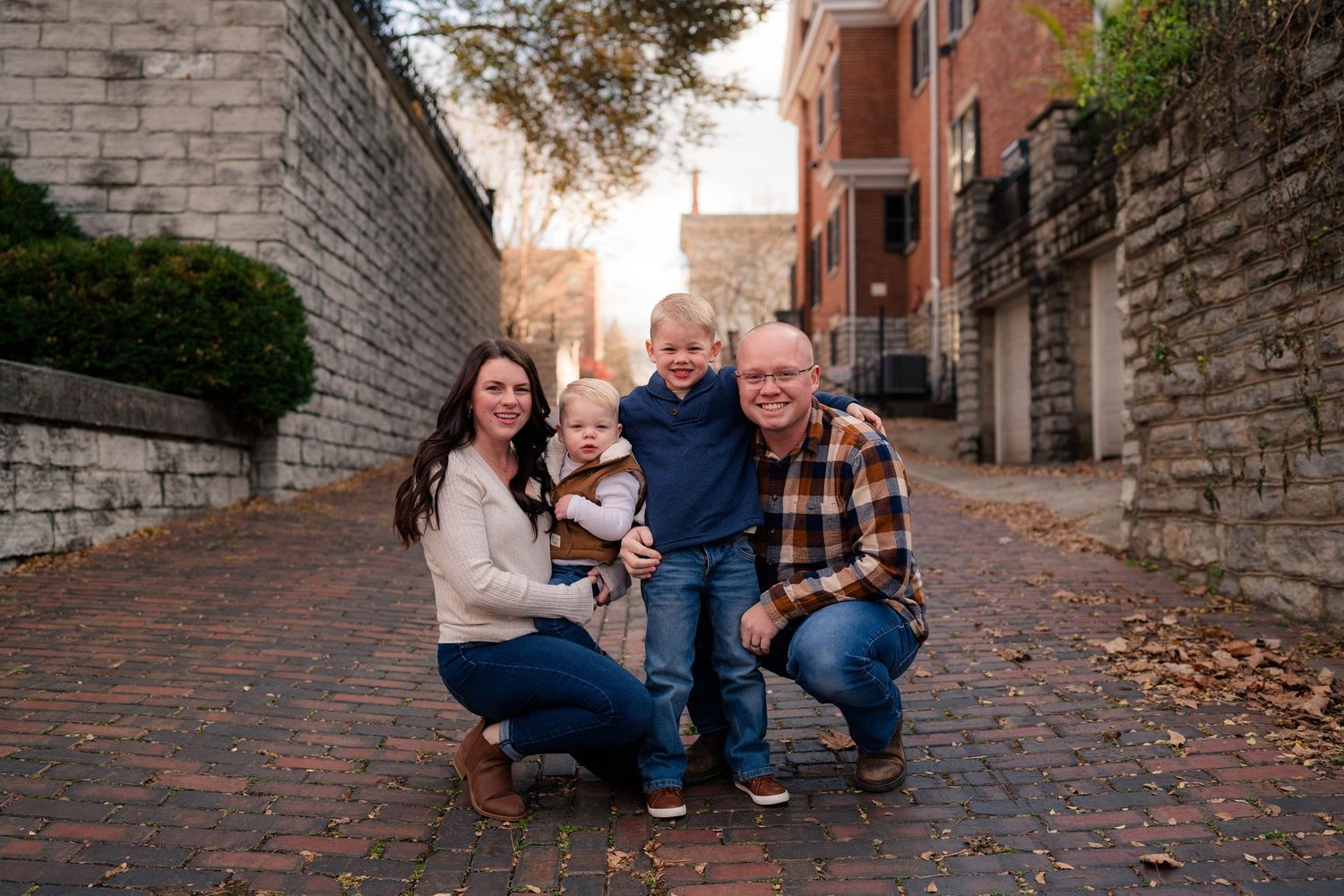 Happy family of four posing on charming brick alley at golden hour with warm sunset light.