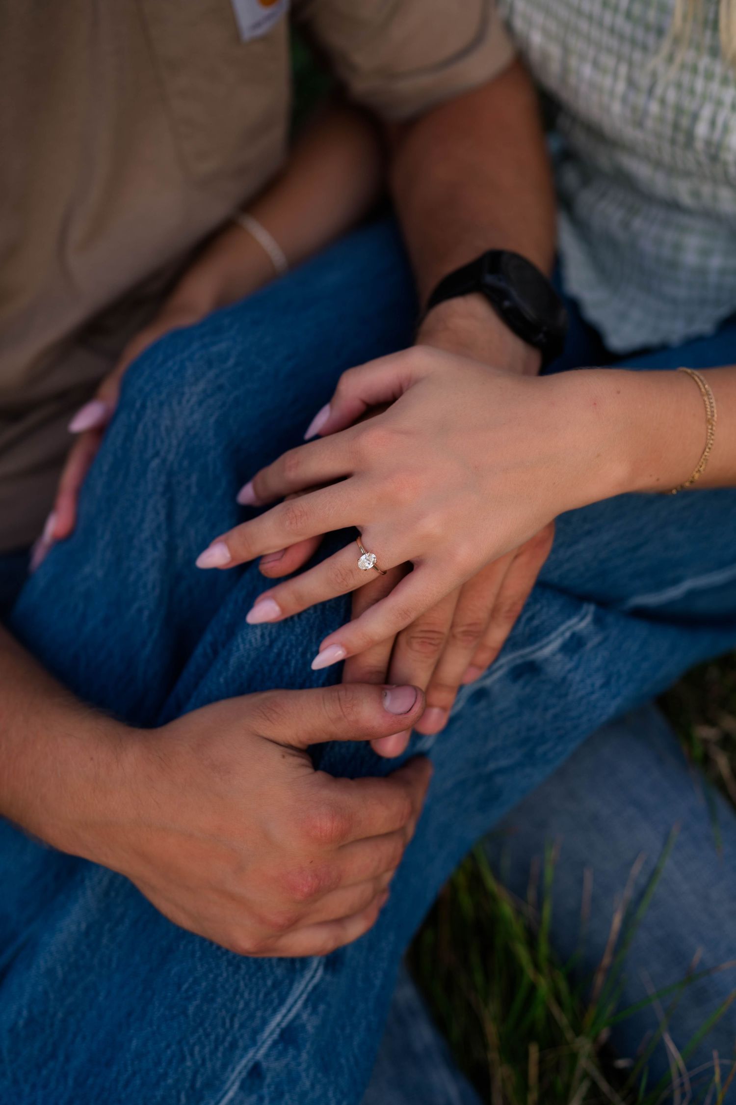 Close-up of a couple holding hands showing an engagement ring, woman wearing jeans and a diamond solitaire ring.