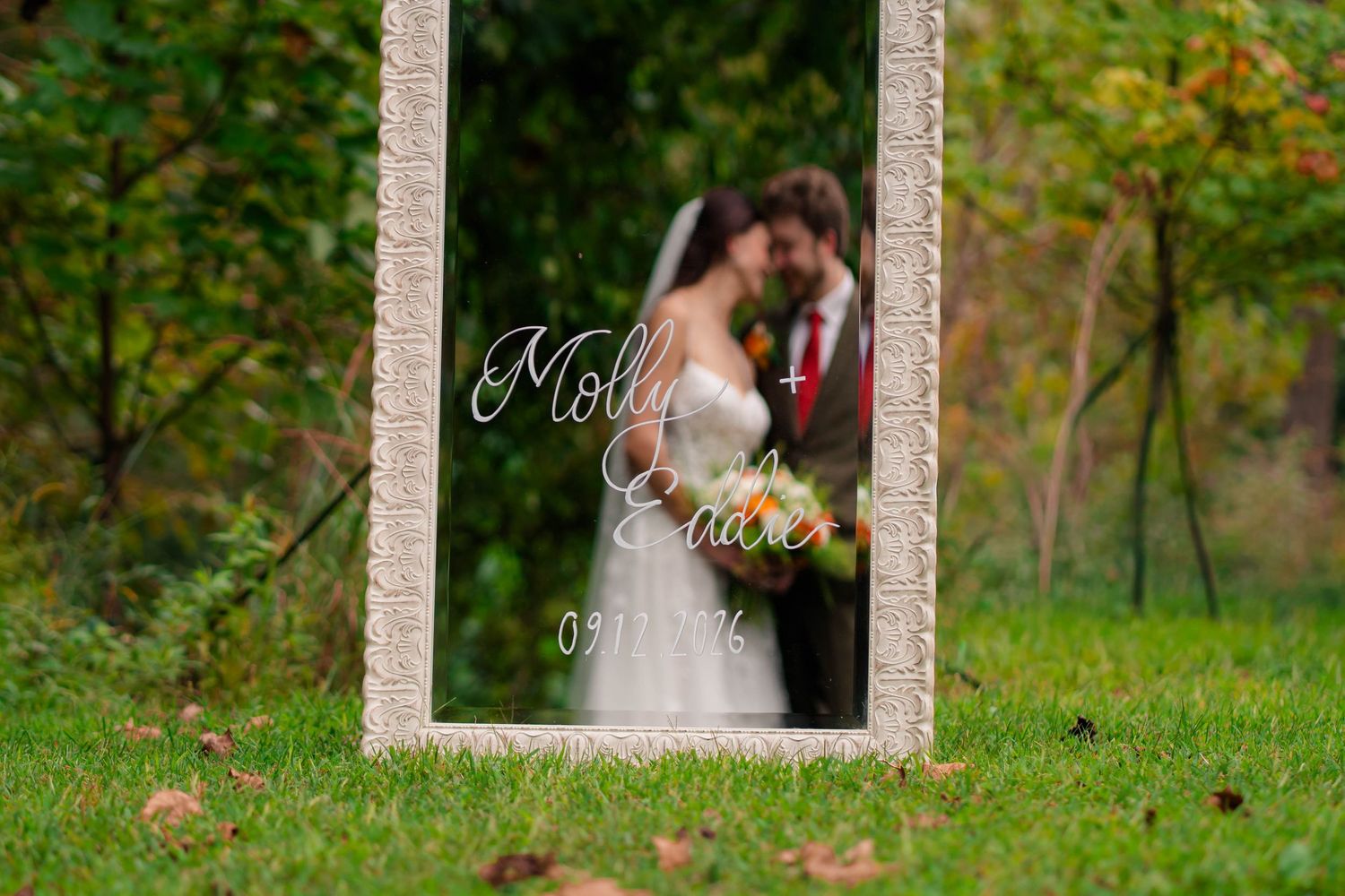Wedding mirror sign reading Molly and Evan with couple kissing reflected in background.