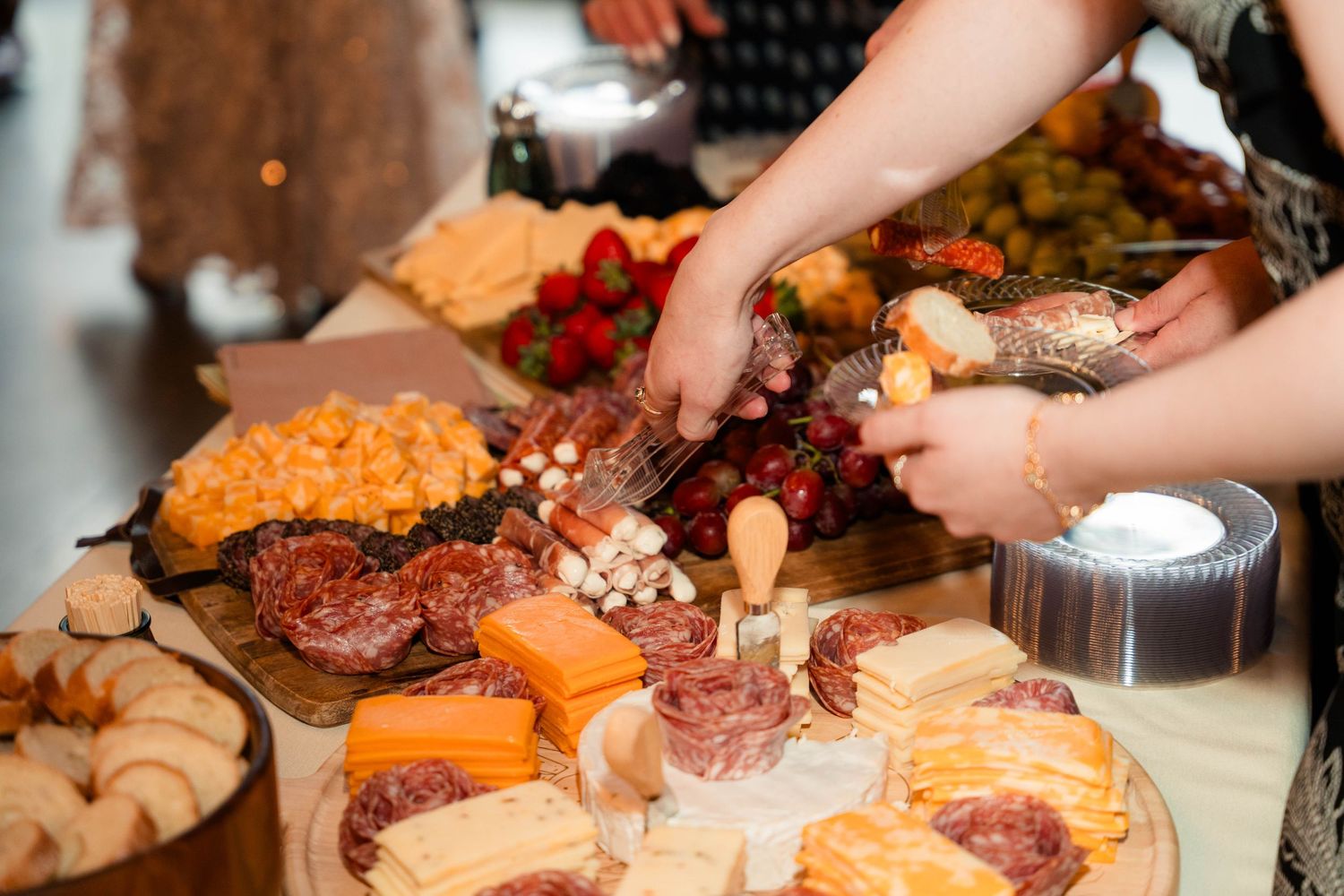 Guests serving themselves from a wedding charcuterie spread with meats, cheeses, and fresh fruit.
