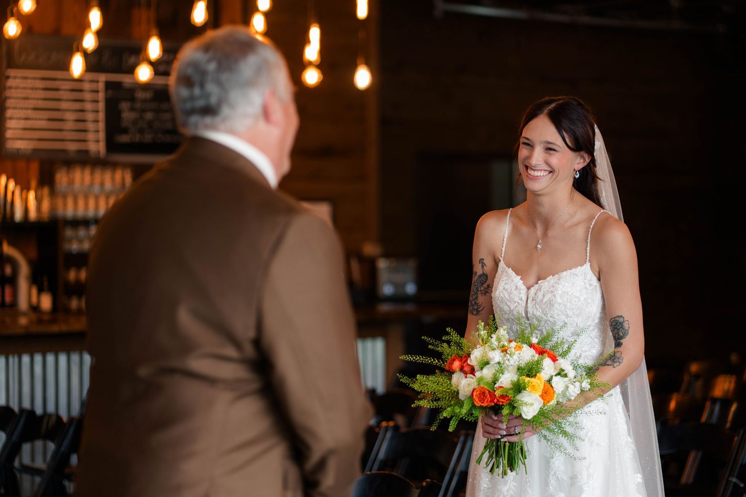 Bride in lace wedding gown holding colorful bouquet smiling at father during first look.
