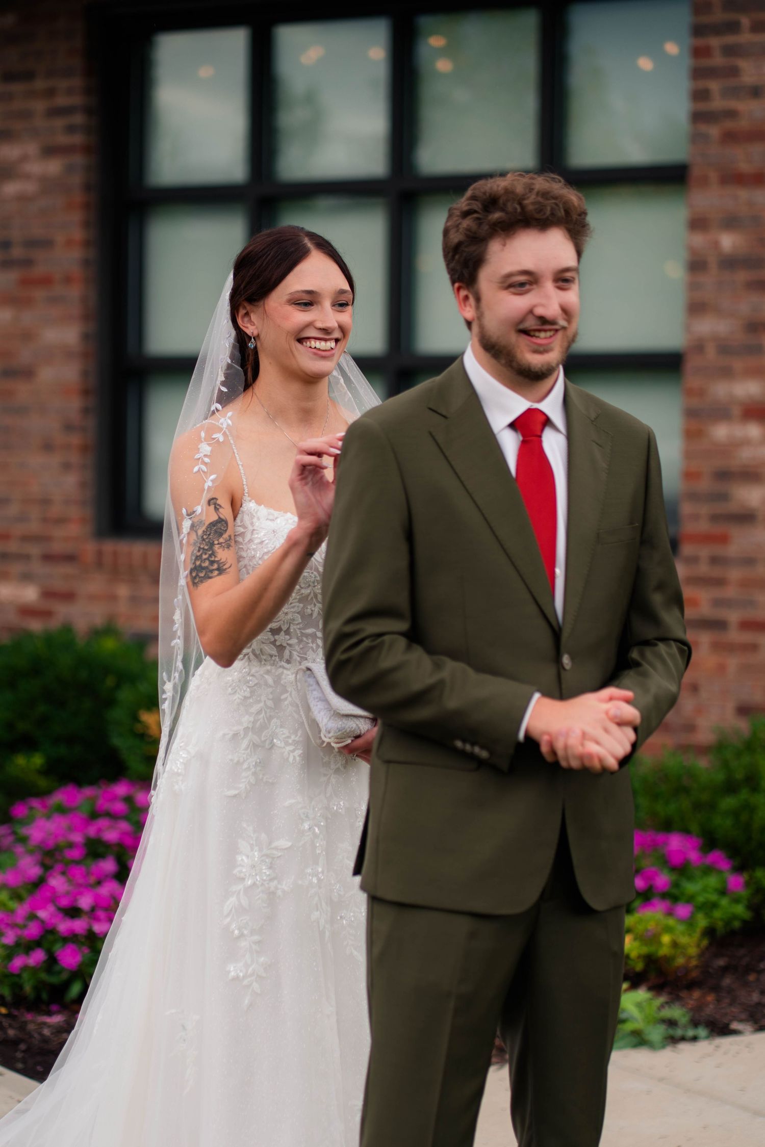 Smiling bride and groom share first look moment outside brick building on wedding day.