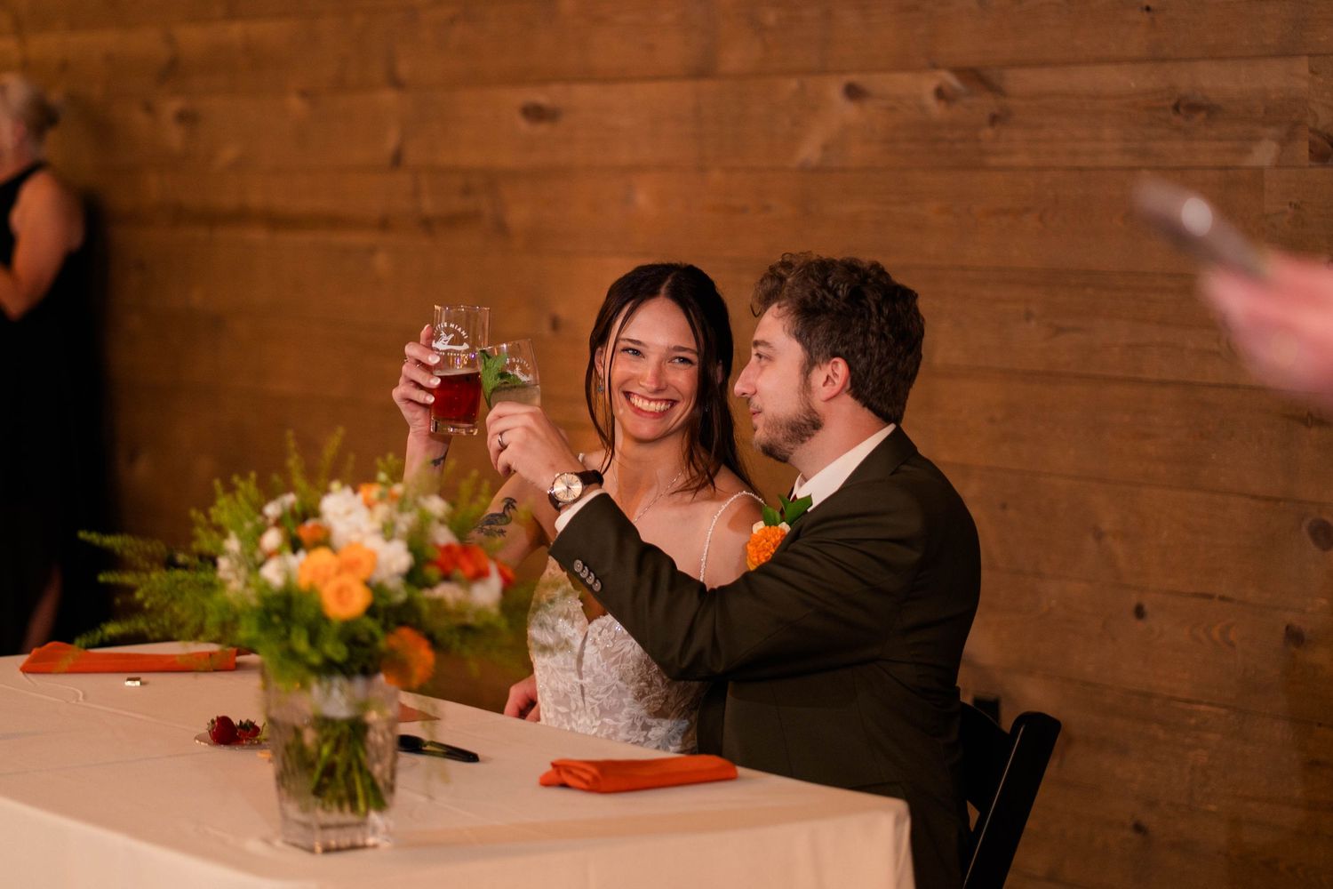 Bride and groom toast with drinks at sweetheart table during wedding reception.