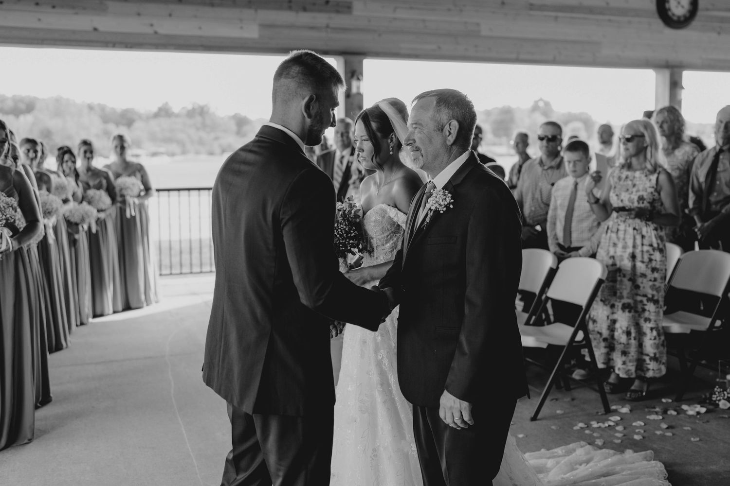 Black and white photo of a groom receiving the bride from her father at a wedding ceremony.