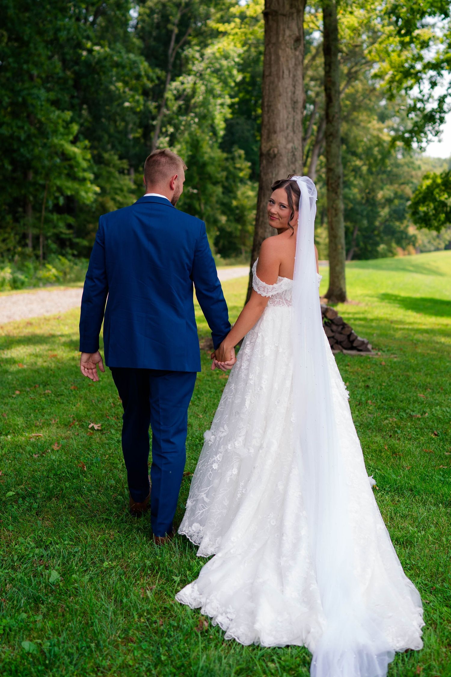Bride and groom walking hand in hand through lush green park on their wedding day.