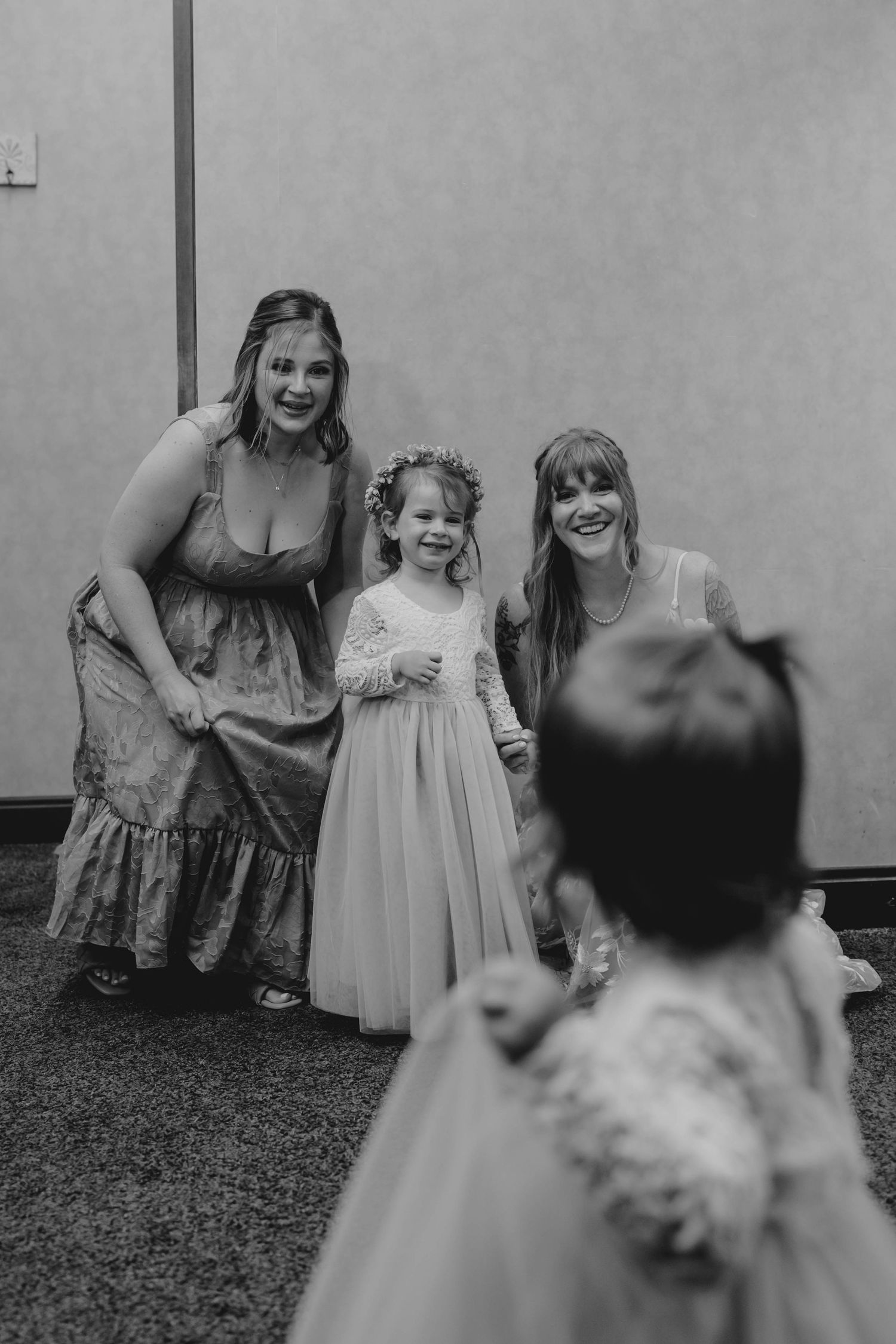 Black and white photo of two bridesmaids smiling at flower girls in white dresses at a wedding.