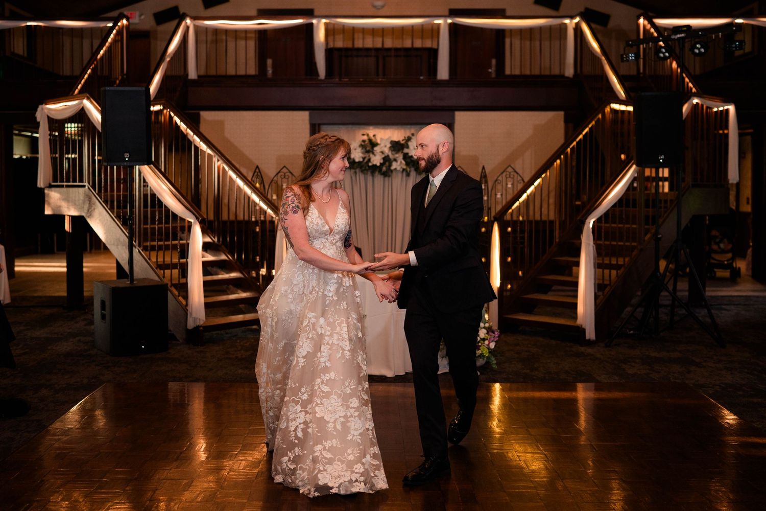 Bride and groom hold hands facing each other on dance floor at wedding reception.